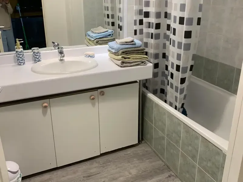 Salle de bain avec vanité blanche, lavabo, serviettes et rideau de douche à motifs carrés au-dessus d'une baignoire.