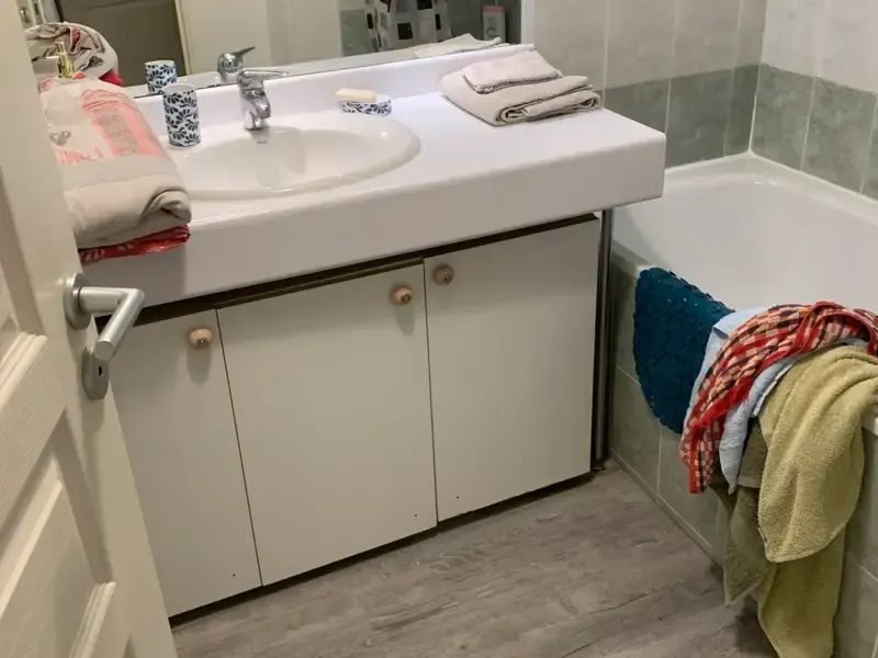 Salle de bain avec lavabo blanc, meubles de rangement et baignoire. Serviettes fournies.