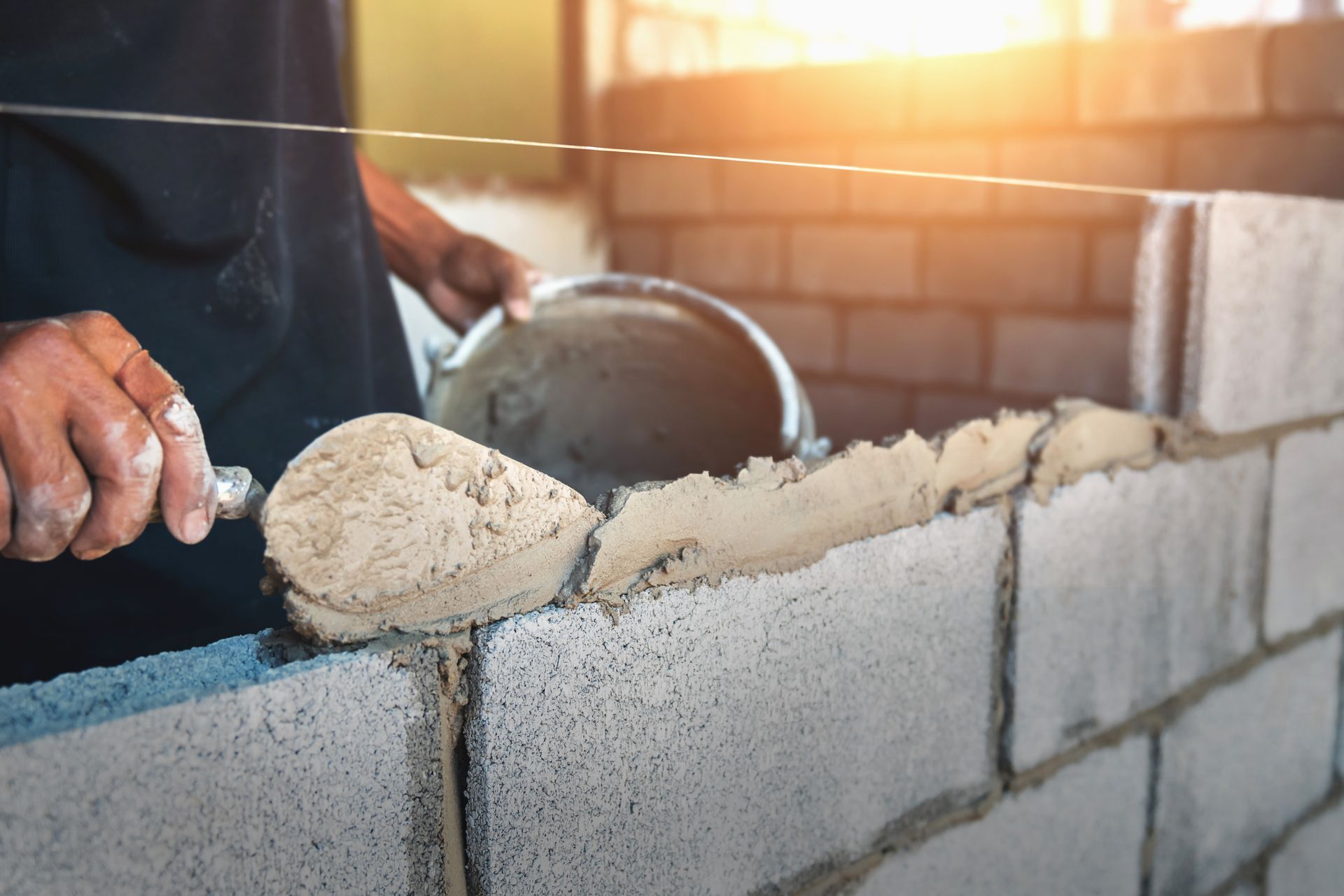 Des mains étalent du mortier sur un mur en parpaings sur un chantier de construction