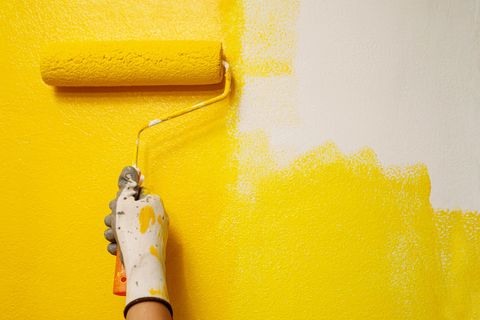 Peinture d'un mur à la main en jaune vif avec un rouleau à peinture