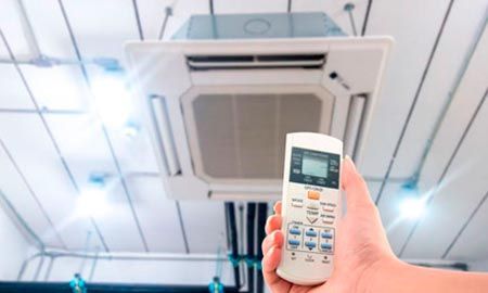 Una persona sostiene un control remoto frente a un acondicionador de aire.