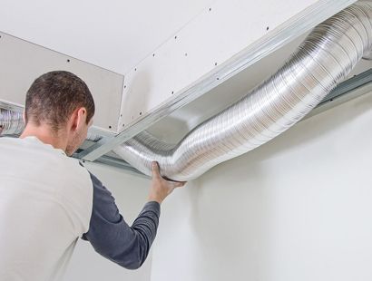 Un hombre está instalando un conducto de aire desde el techo.