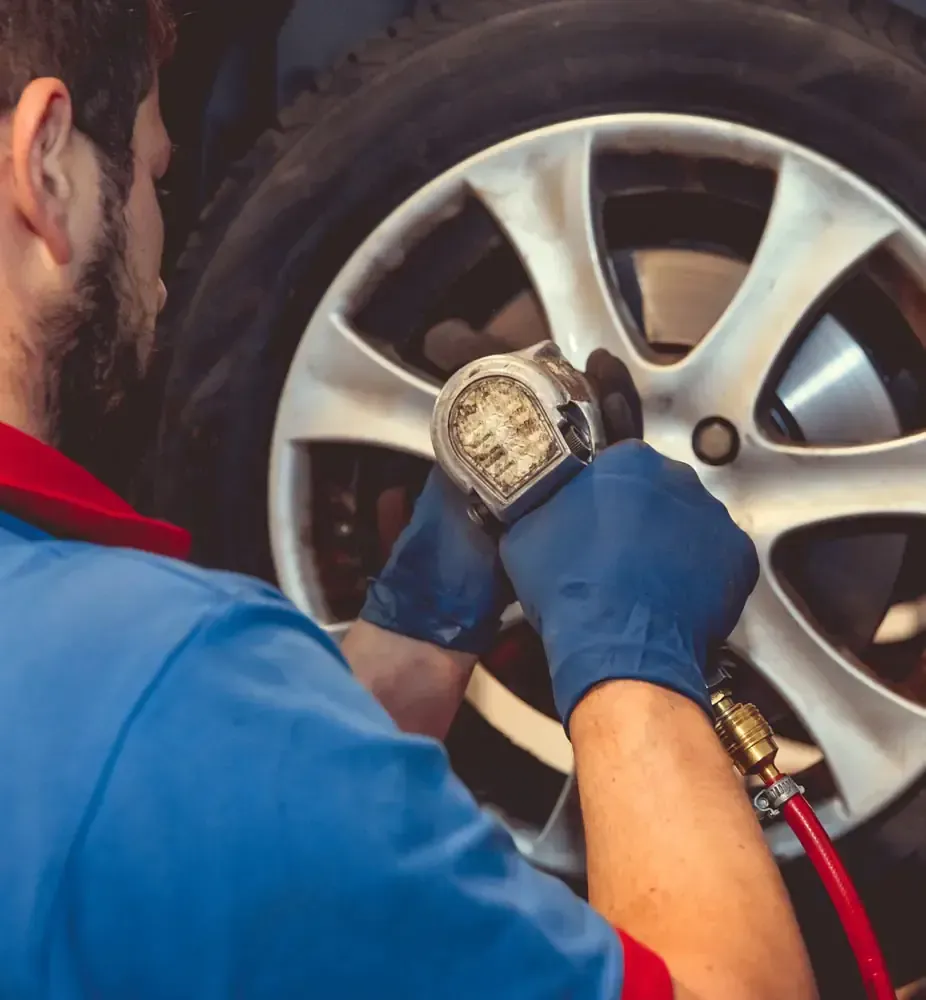 Un mecánico con guantes azules infla un neumático con un manómetro. La manguera roja está conectada a la herramienta.