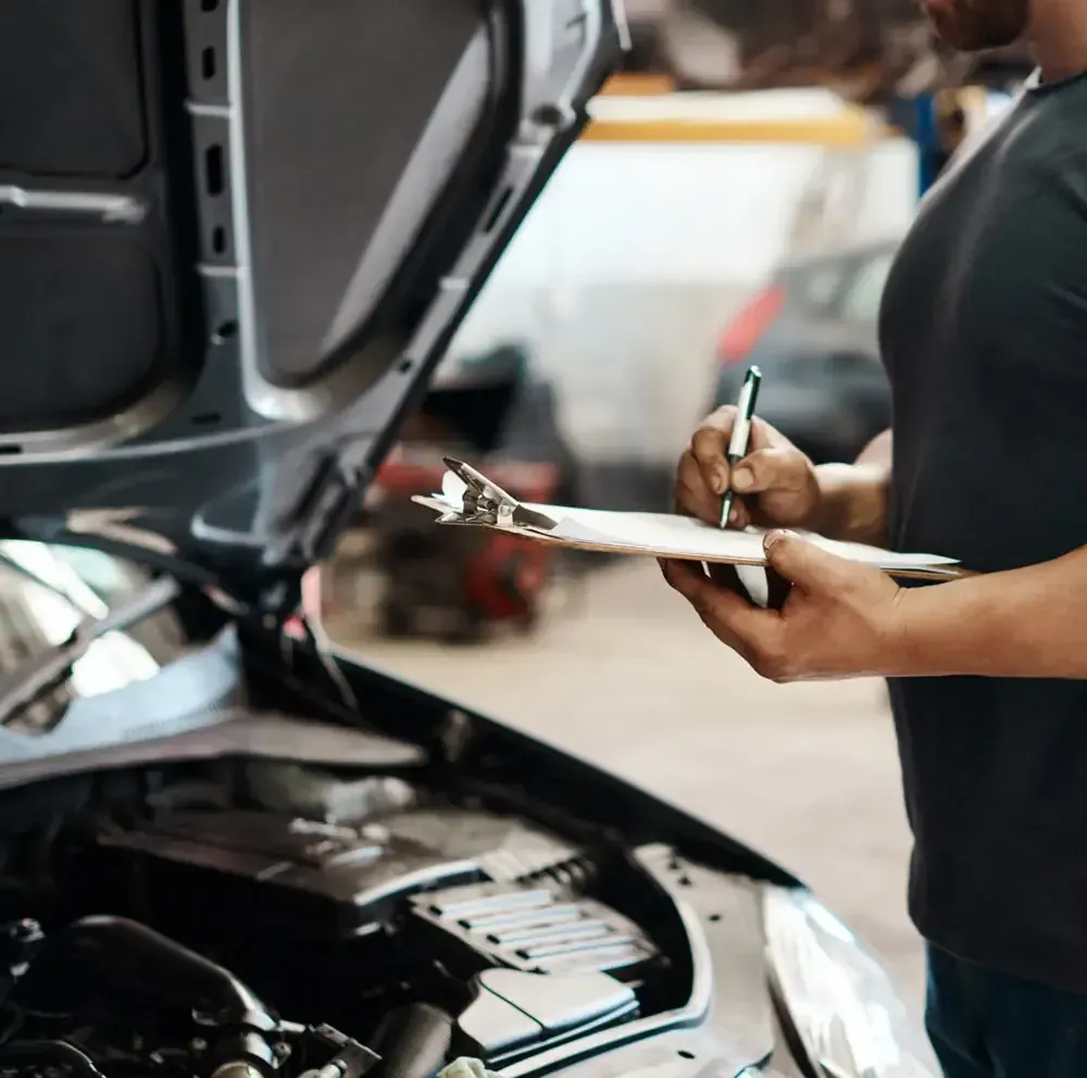Mecánico con portapapeles inspeccionando el motor del coche en un garaje.