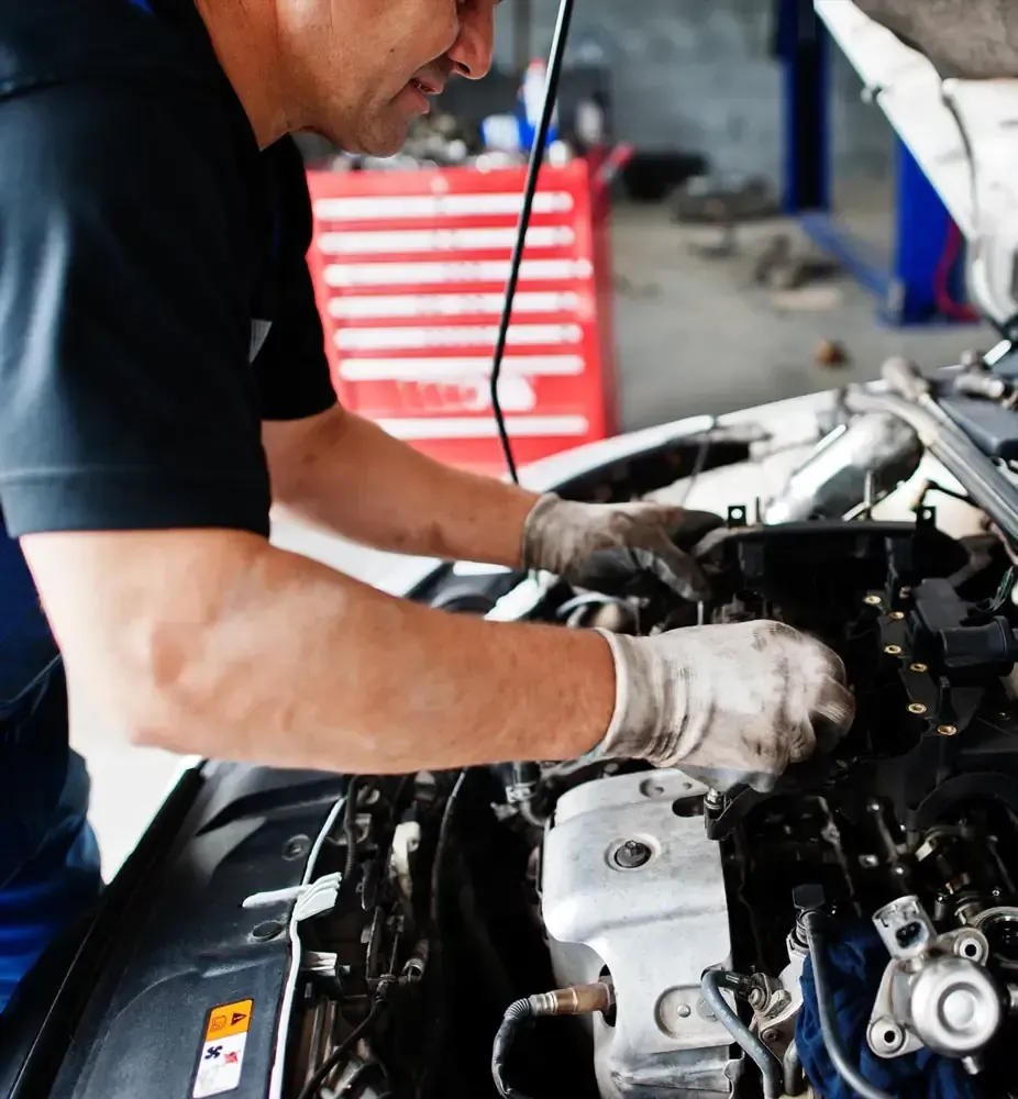 Mecánico trabajando en un motor de coche en un taller de reparación, usando guantes.