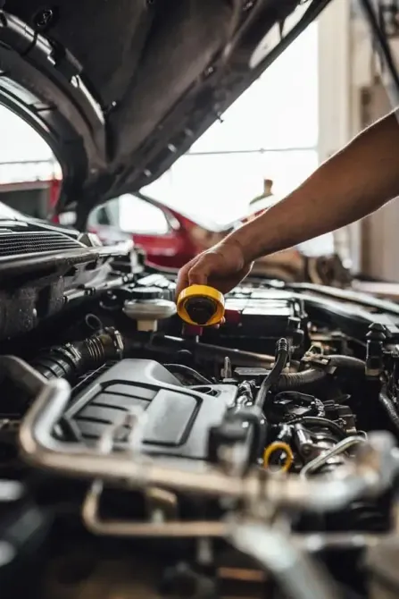Persona añadiendo aceite al motor de un coche en un garaje.