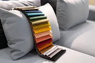 Muestras de tela en varios colores distribuidas en abanico sobre un sofá gris y almohadas.