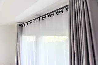 Cortinas grises y blancas colgando de una barra negra frente a una ventana.