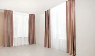 Habitación vacía con dos ventanas cubiertas con cortinas blancas transparentes y cortinas malva.