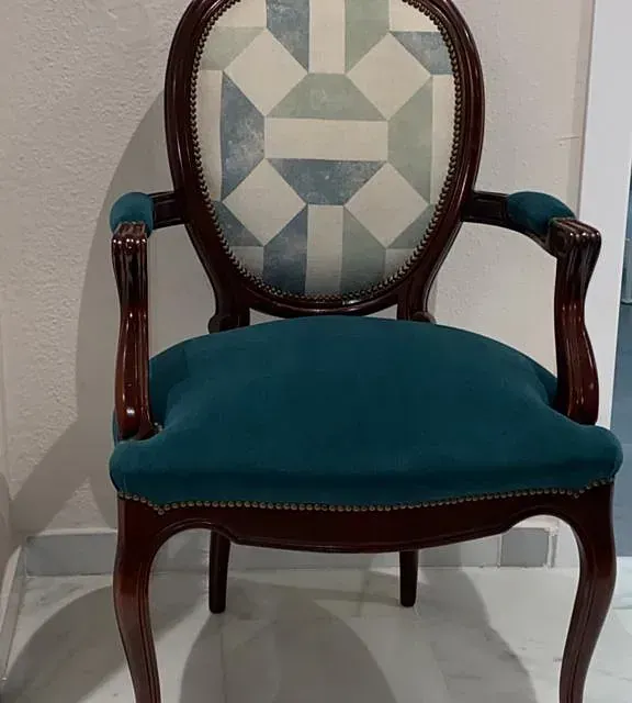 Una silla antigua con asiento y respaldo color verde azulado, respaldo estampado y estructura de madera oscura.