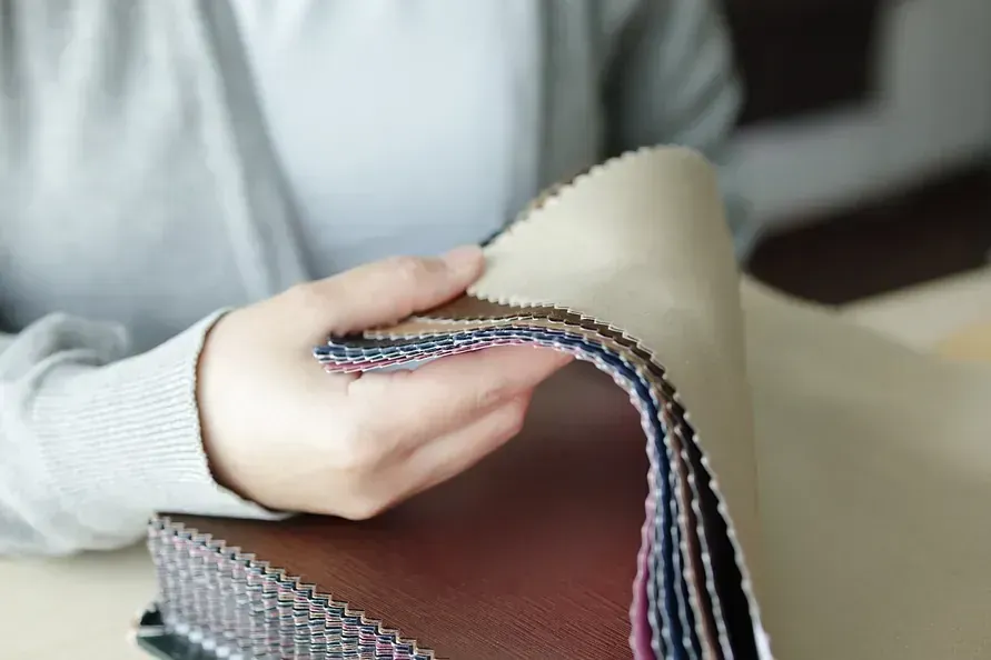 Persona sosteniendo y examinando una pila de muestras de tela, de varios colores y texturas, en el interior.