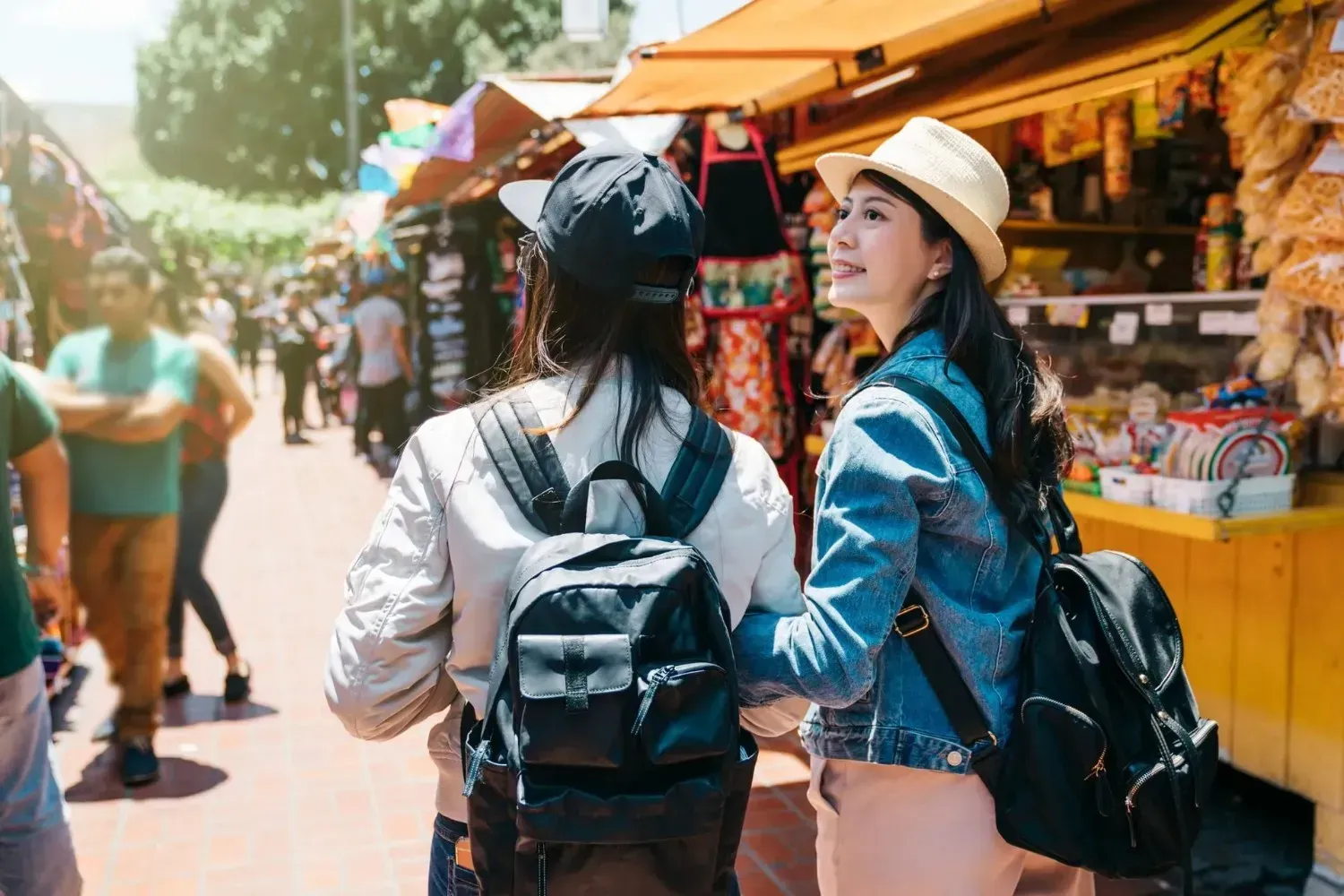 Dos personas con mochilas caminan por un mercado lleno de gente, mirando las tiendas.