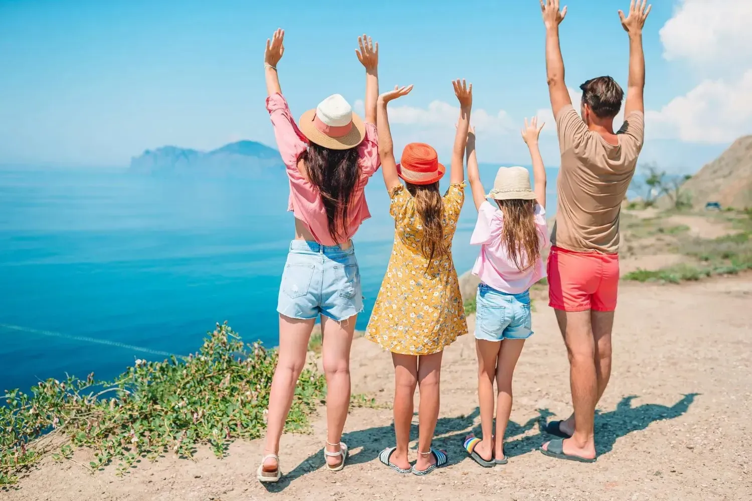 Familia con los brazos en alto, mirando el océano azul desde el acantilado.