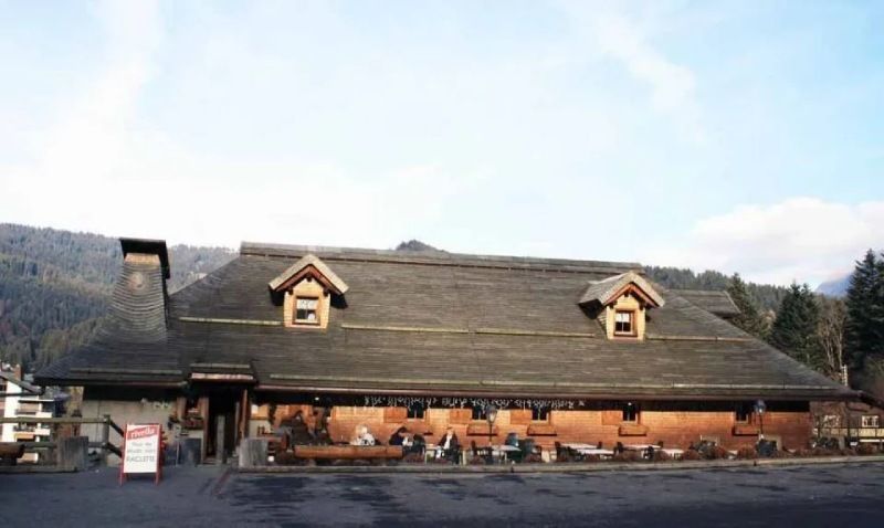 Une grande maison en bois avec un toit de chaume est entourée de montagnes.