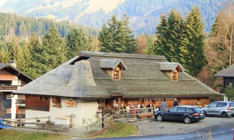 Une maison au toit de chaume est entourée d'arbres et de voitures garées devant elle