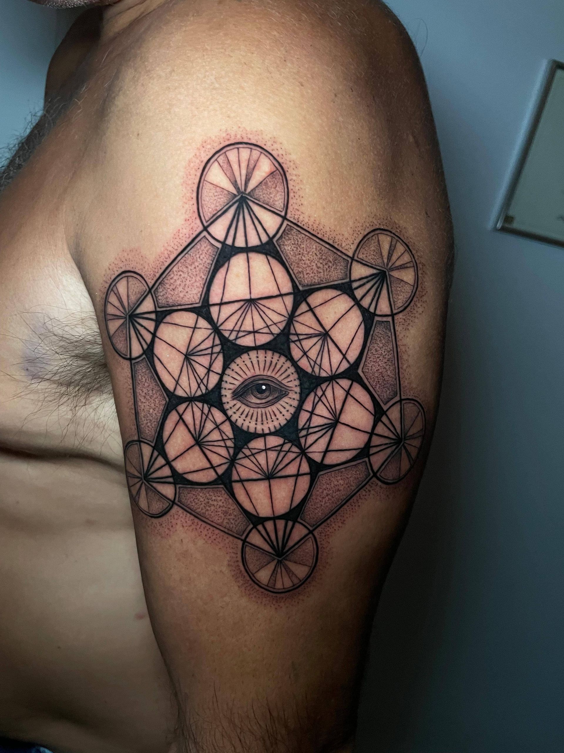 Tatuaje geométrico negro de la flor de la vida en la parte superior del brazo y el hombro de una persona.