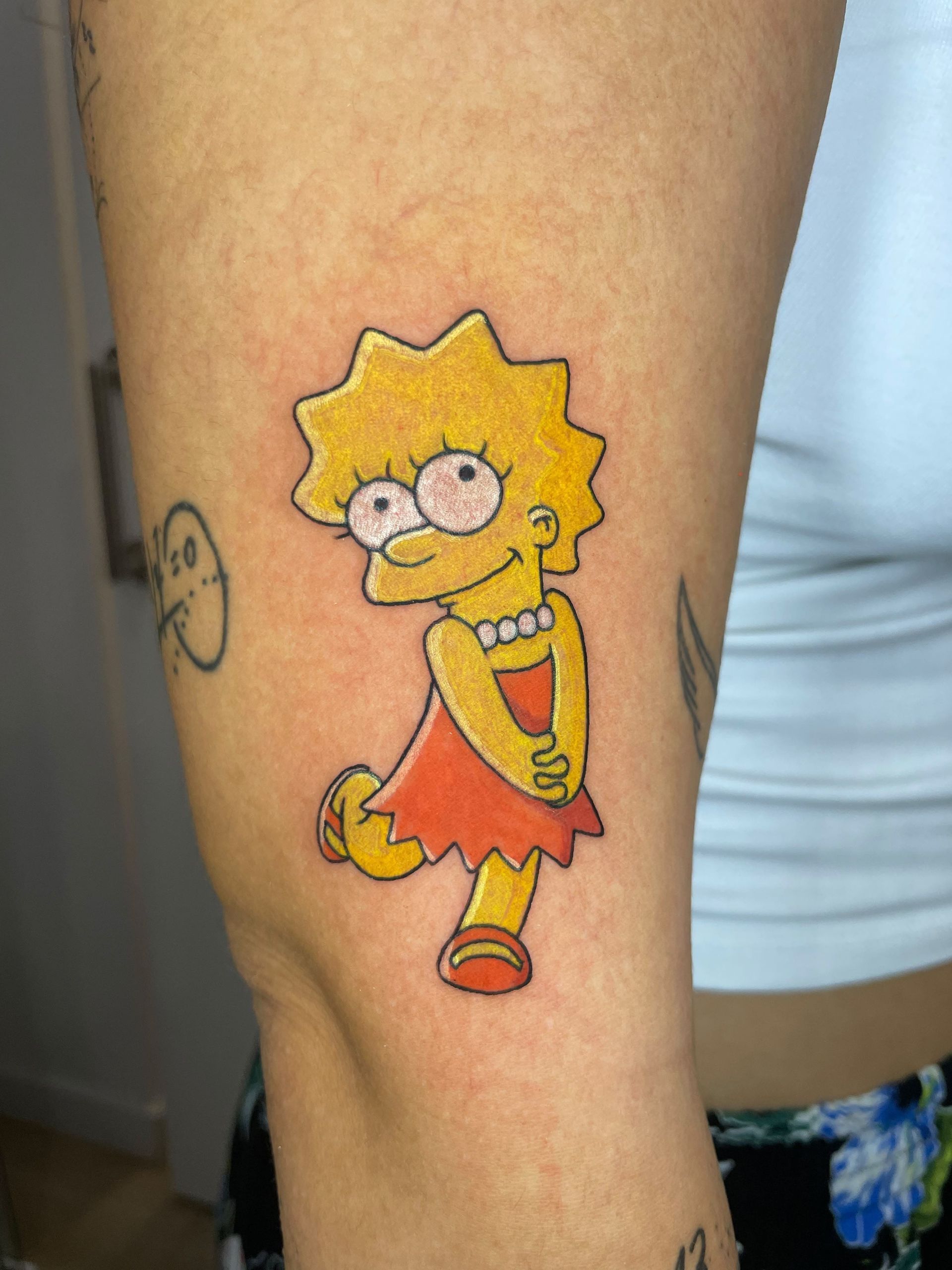 Tatuaje de Lisa Simpson en la pantorrilla de una persona, que la muestra con un vestido rojo y una expresión alegre.