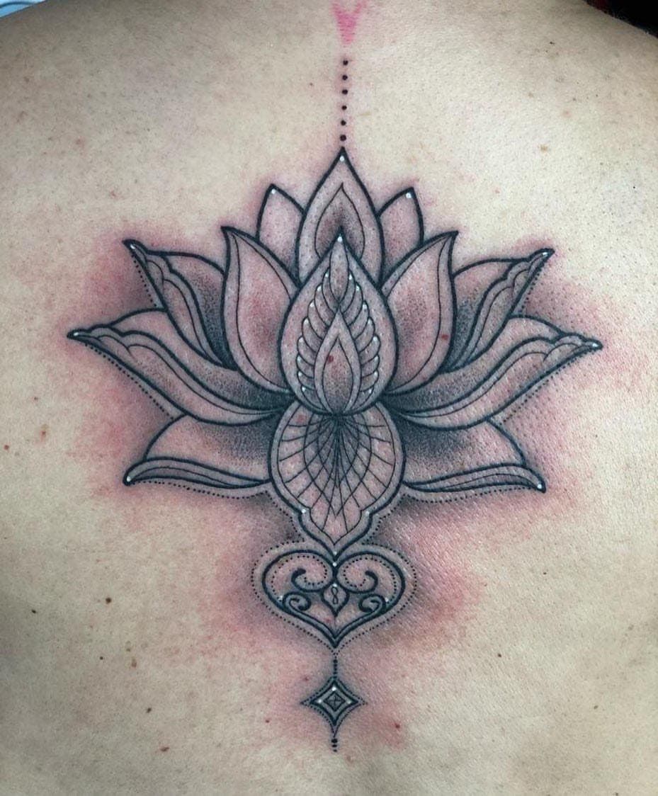 Tatuaje de loto negro con línea vertical punteada y diseño ornamental de corazón y diamante en la piel.