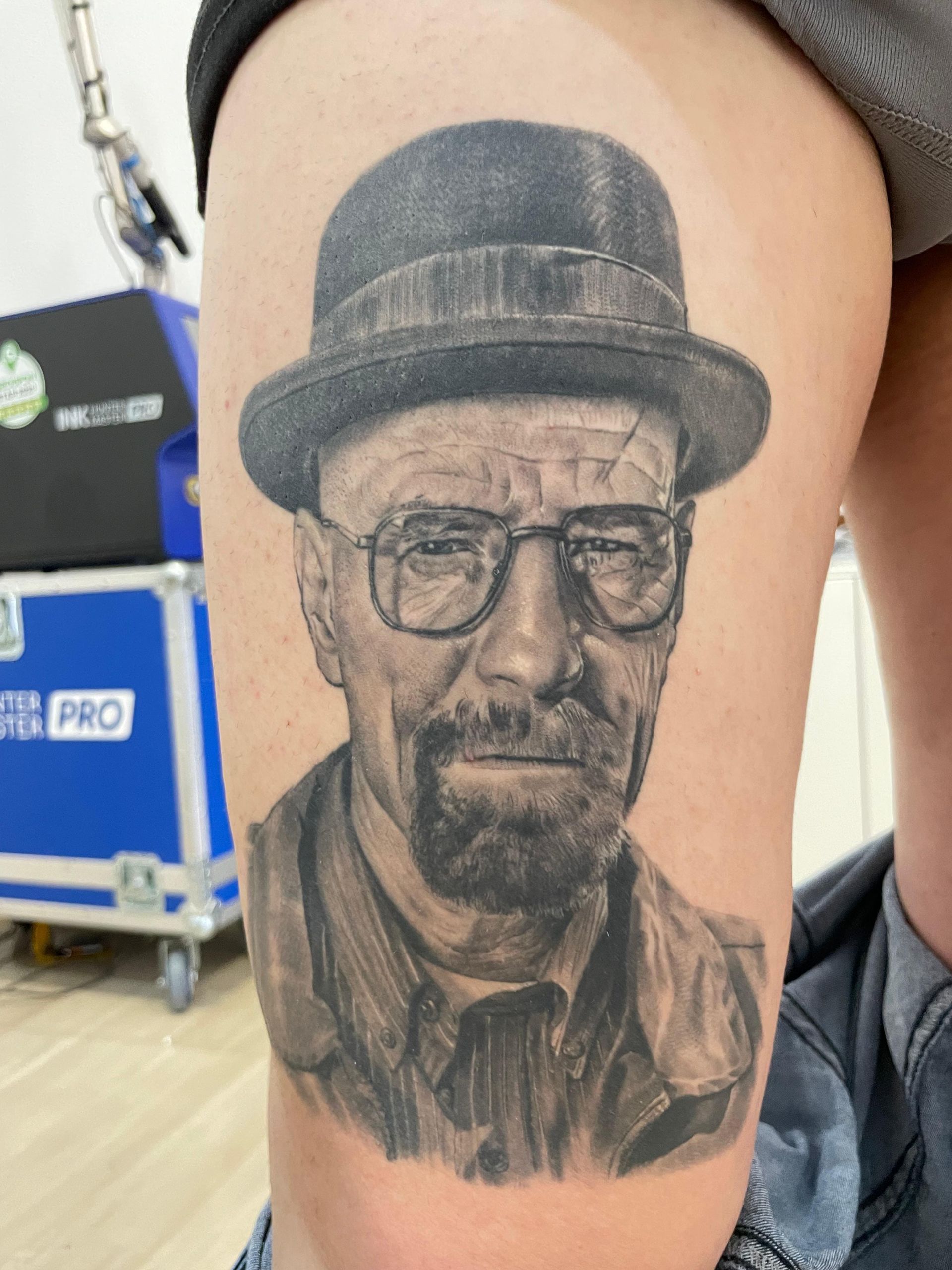 Tatuaje con el retrato de un hombre con sombrero y gafas en la parte superior del brazo.