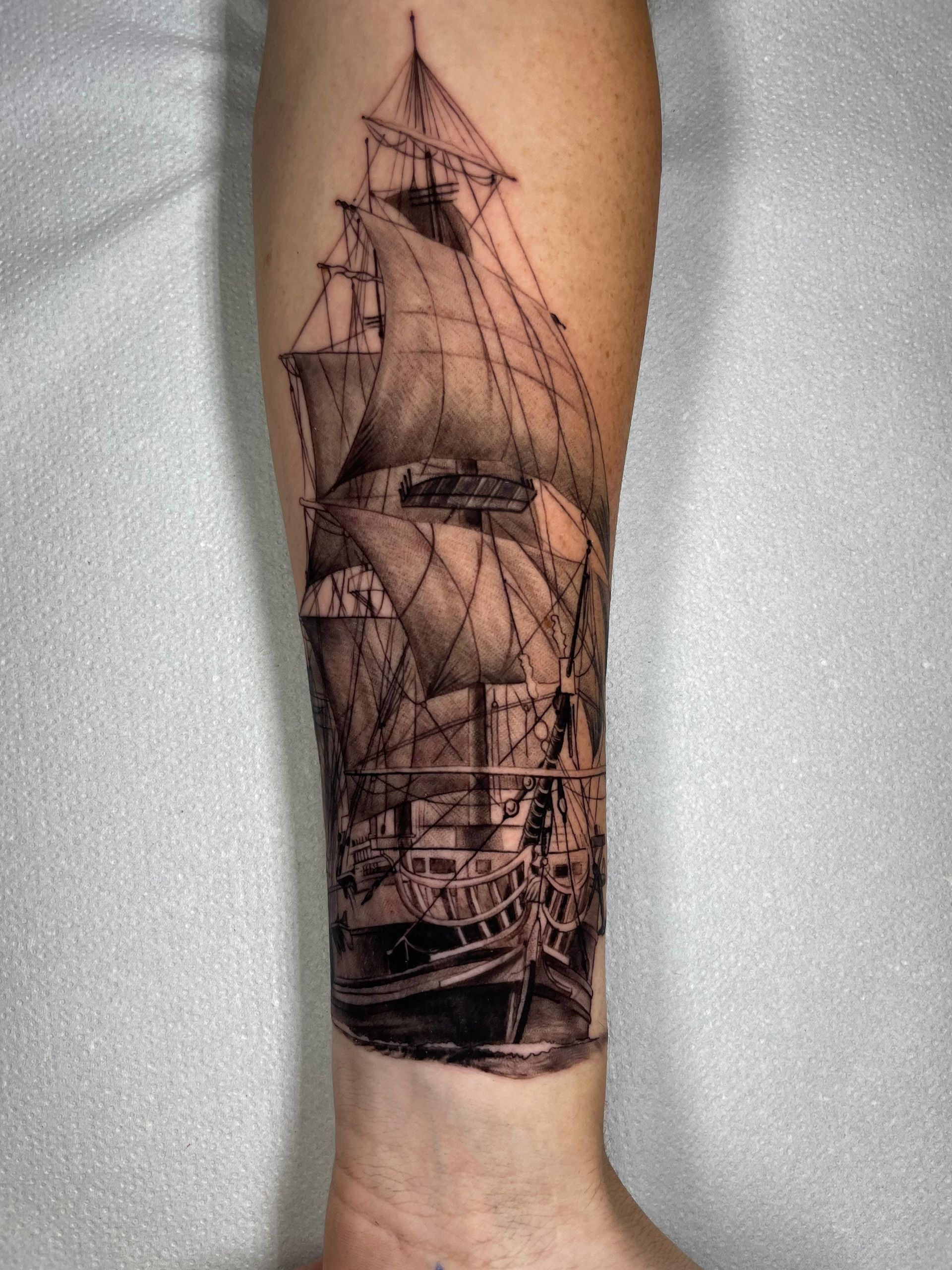 Tatuaje de un barco en blanco y negro en el antebrazo, con velas y aparejos detallados.
