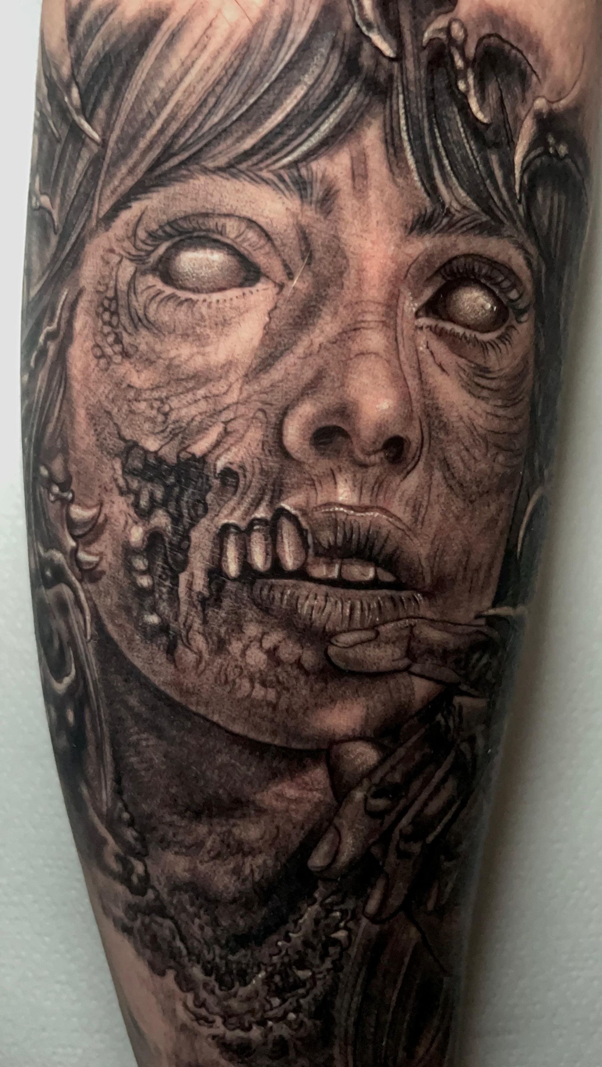 Primer plano de un tatuaje en blanco y negro de un rostro descompuesto, parecido al de un zombi, con ojos huecos y dientes expuestos.
