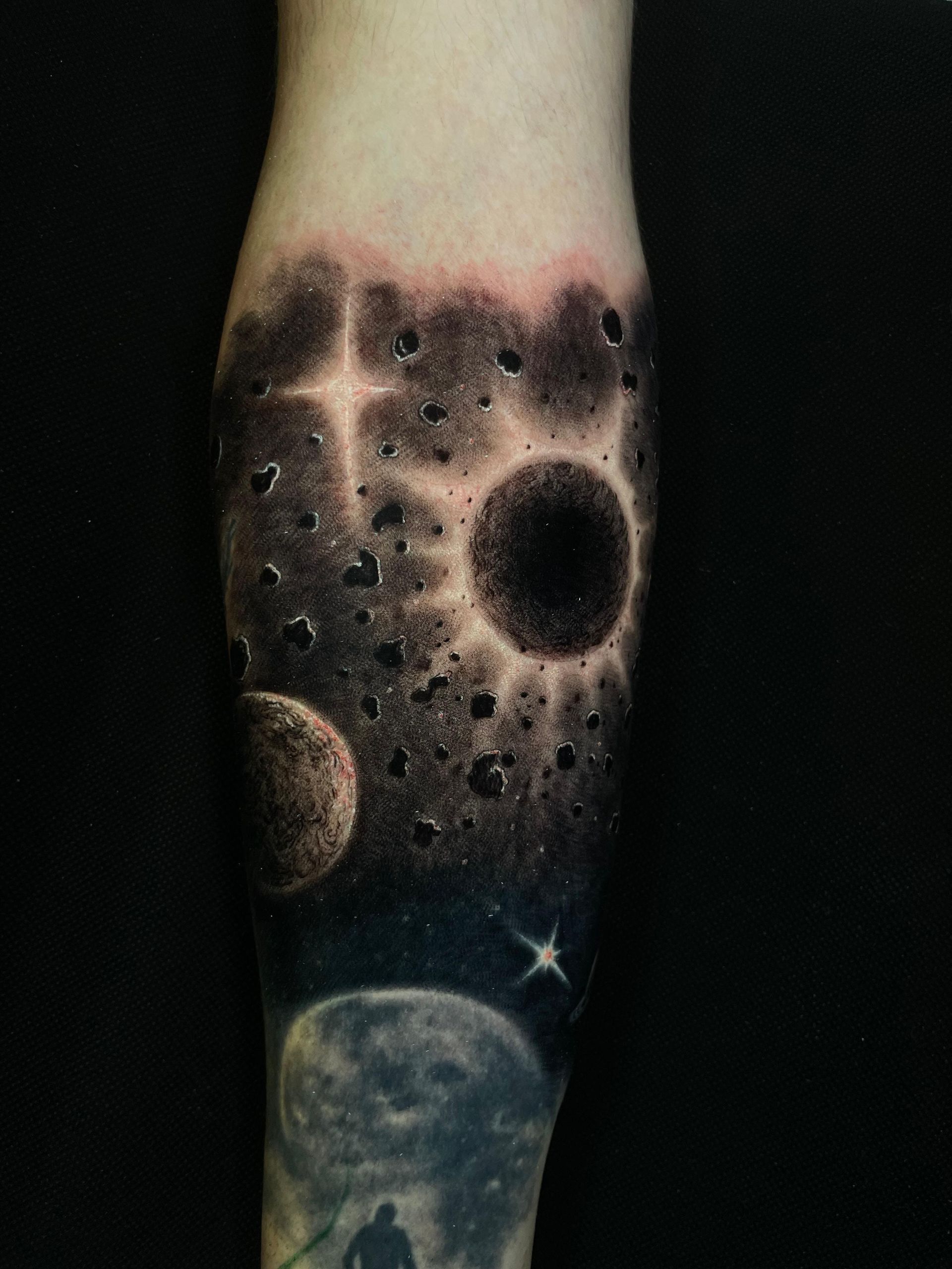 Tatuaje de manga con temática espacial: planetas, estrellas y una luna oscura en el antebrazo.