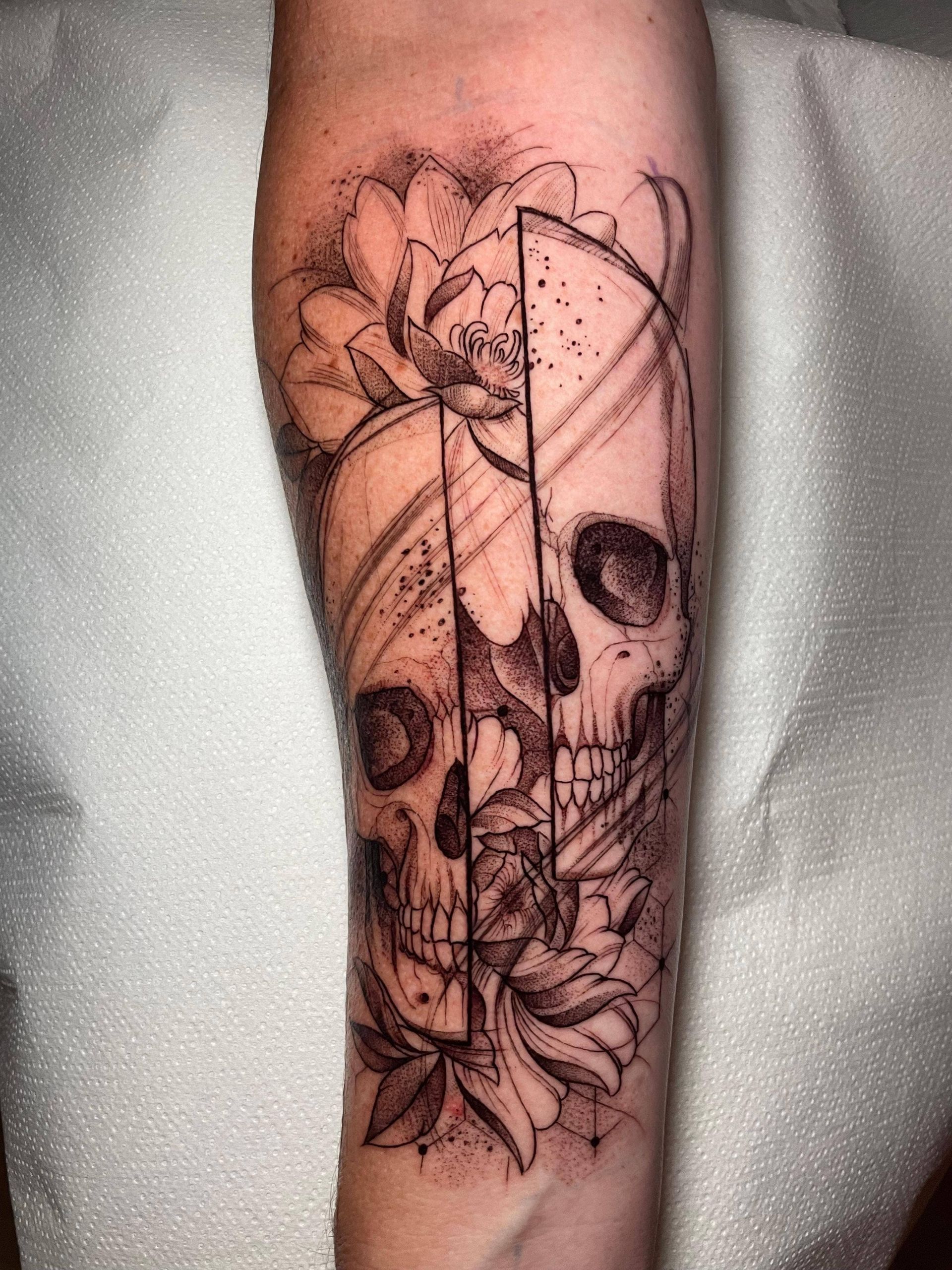 Tatuaje en blanco y negro de una calavera con flores en el antebrazo.
