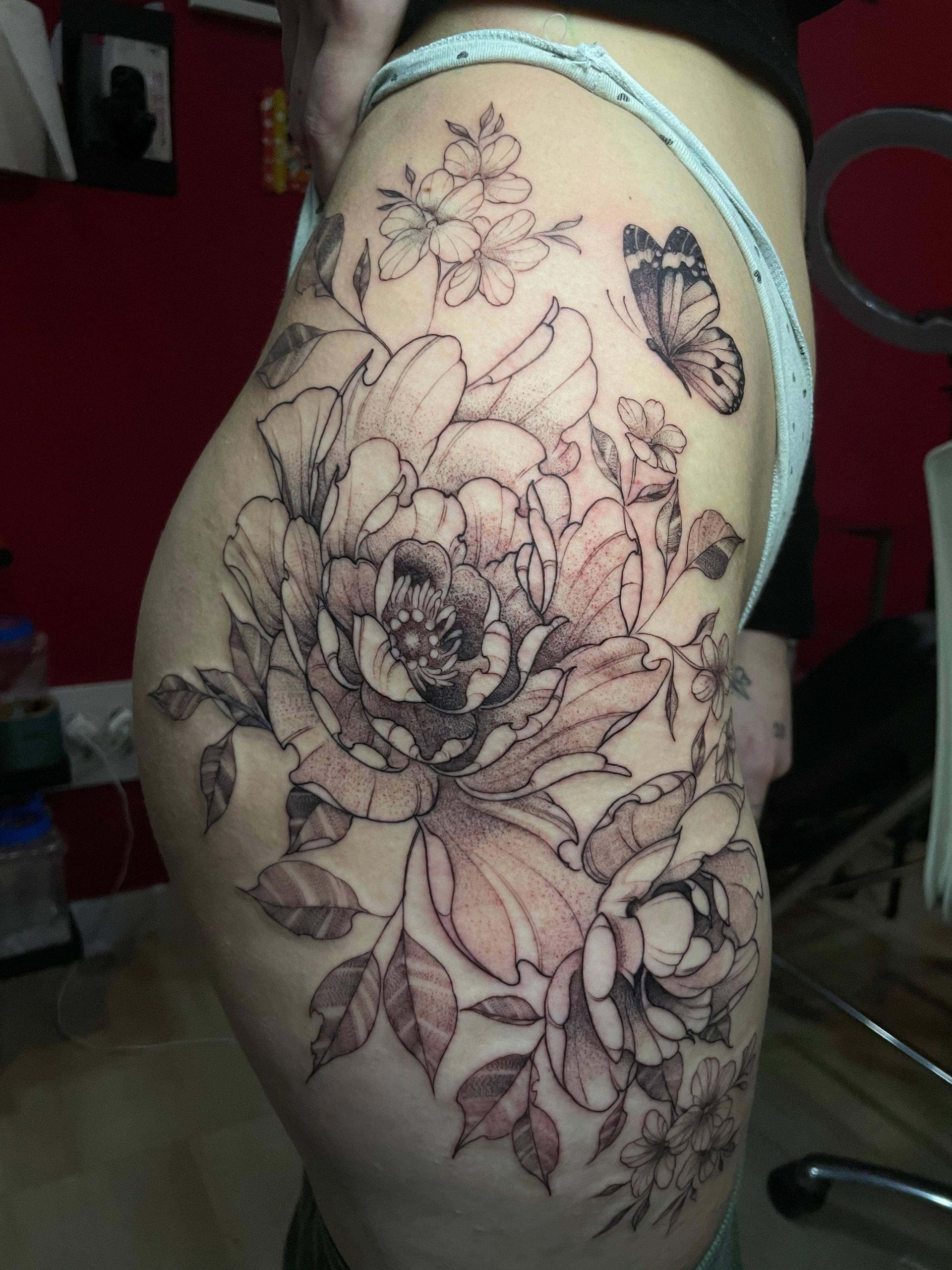 Diseño de tatuaje floral en el muslo de una persona en tinta blanca y negra.