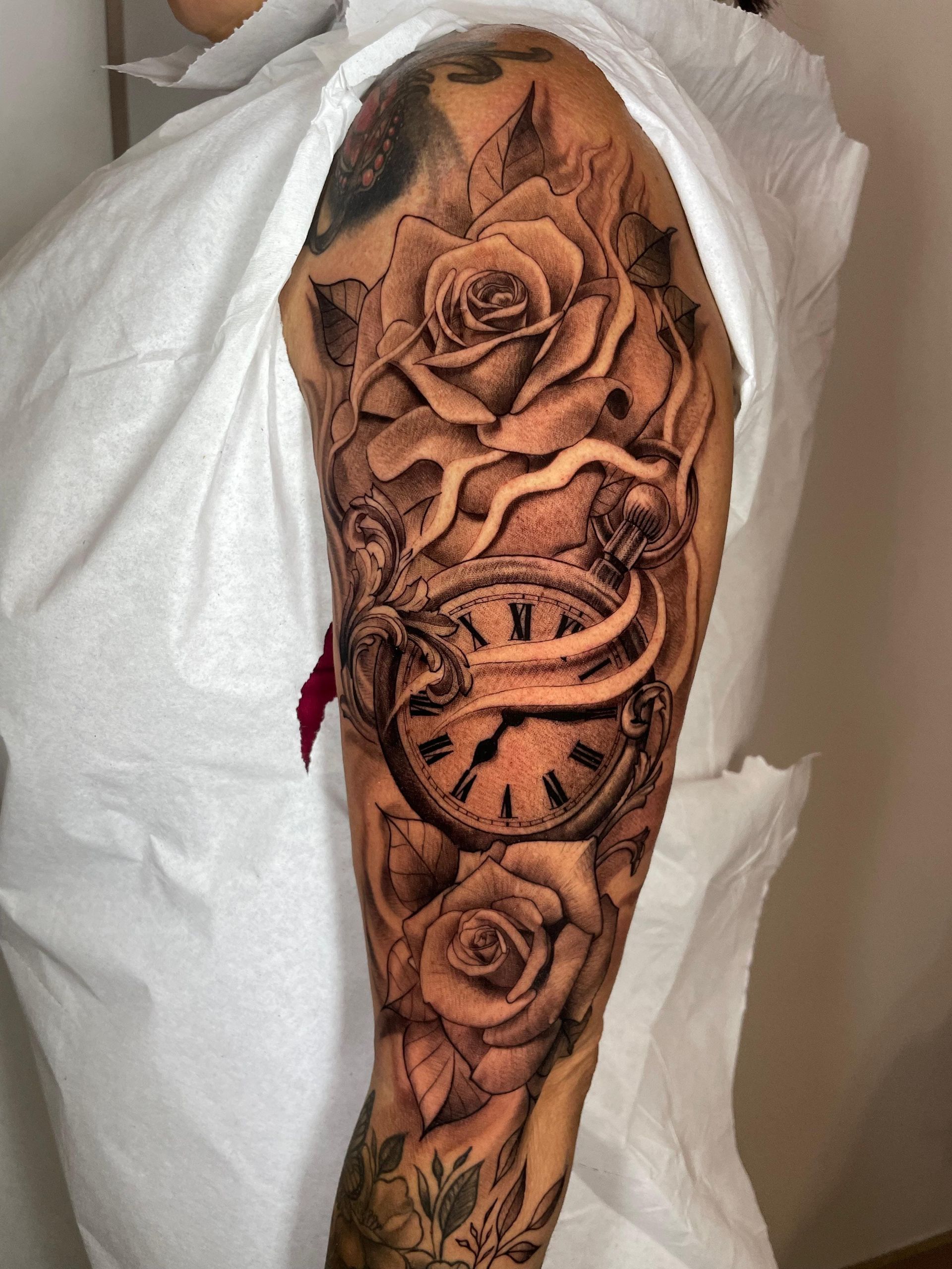 Primer plano de un antebrazo tatuado con grandes diseños florales y de serpientes en tinta negra y marrón.