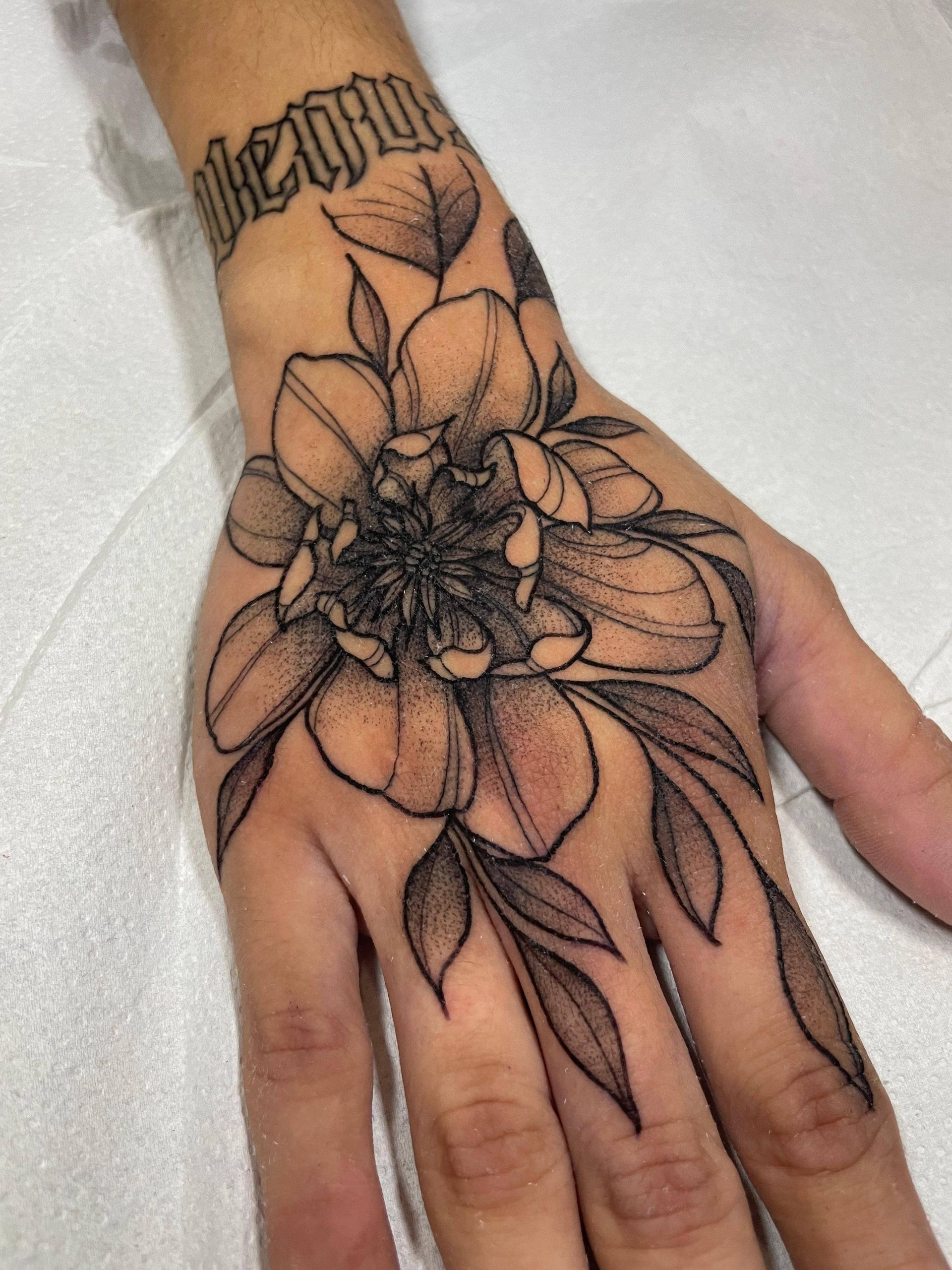 Primer plano de una mano con un tatuaje floral negro en el dorso y la muñeca.