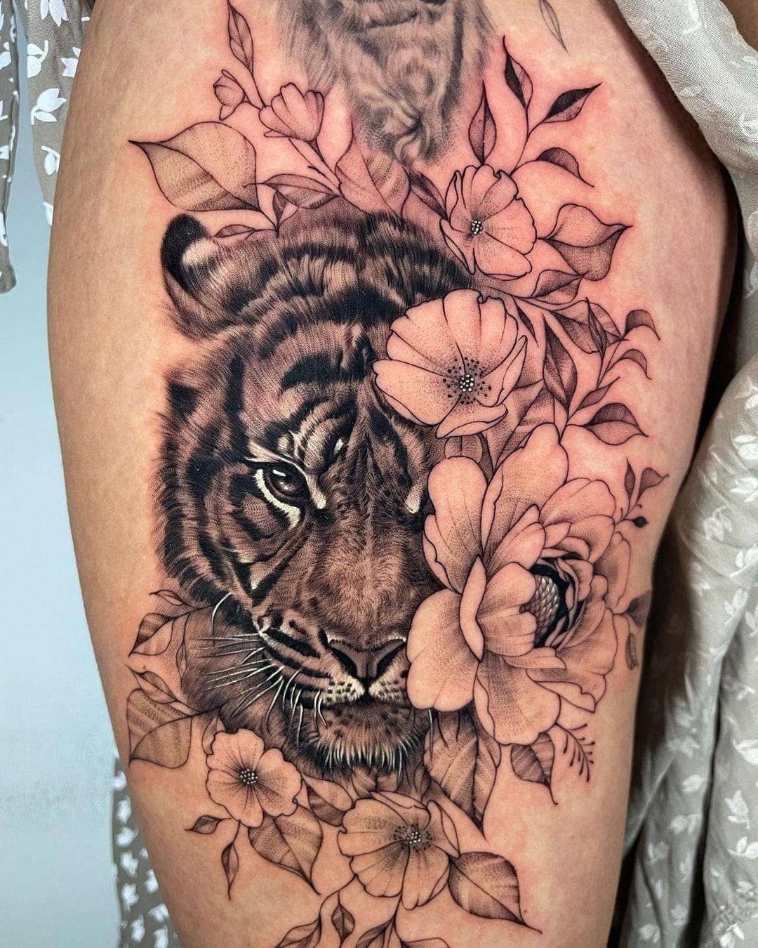 Tatuaje de tigre en blanco y negro rodeado de hojas florales en la piel.