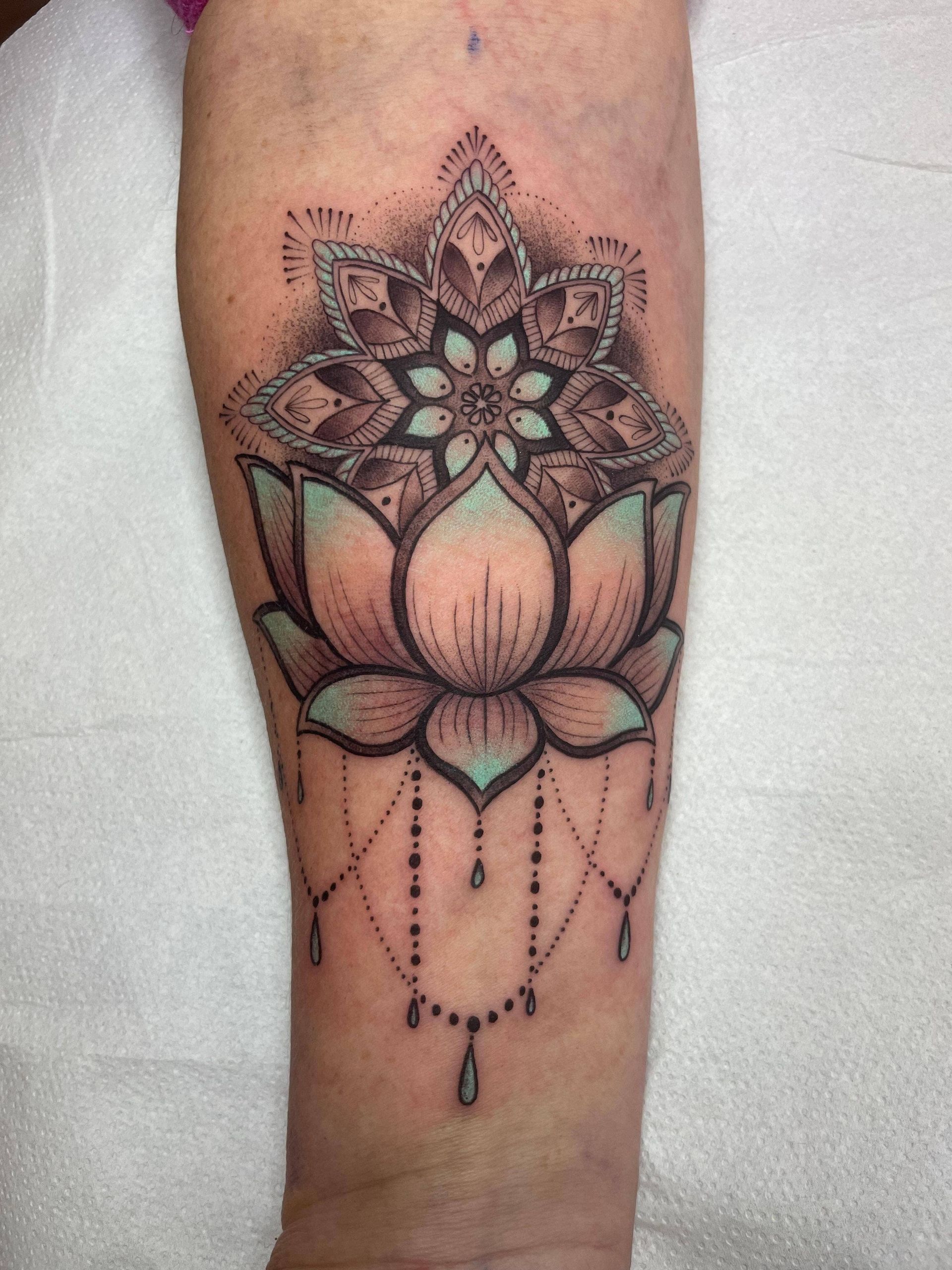 Primer plano de un tatuaje en el antebrazo con un mandala floral y un loto rosa con detalles de cuentas.