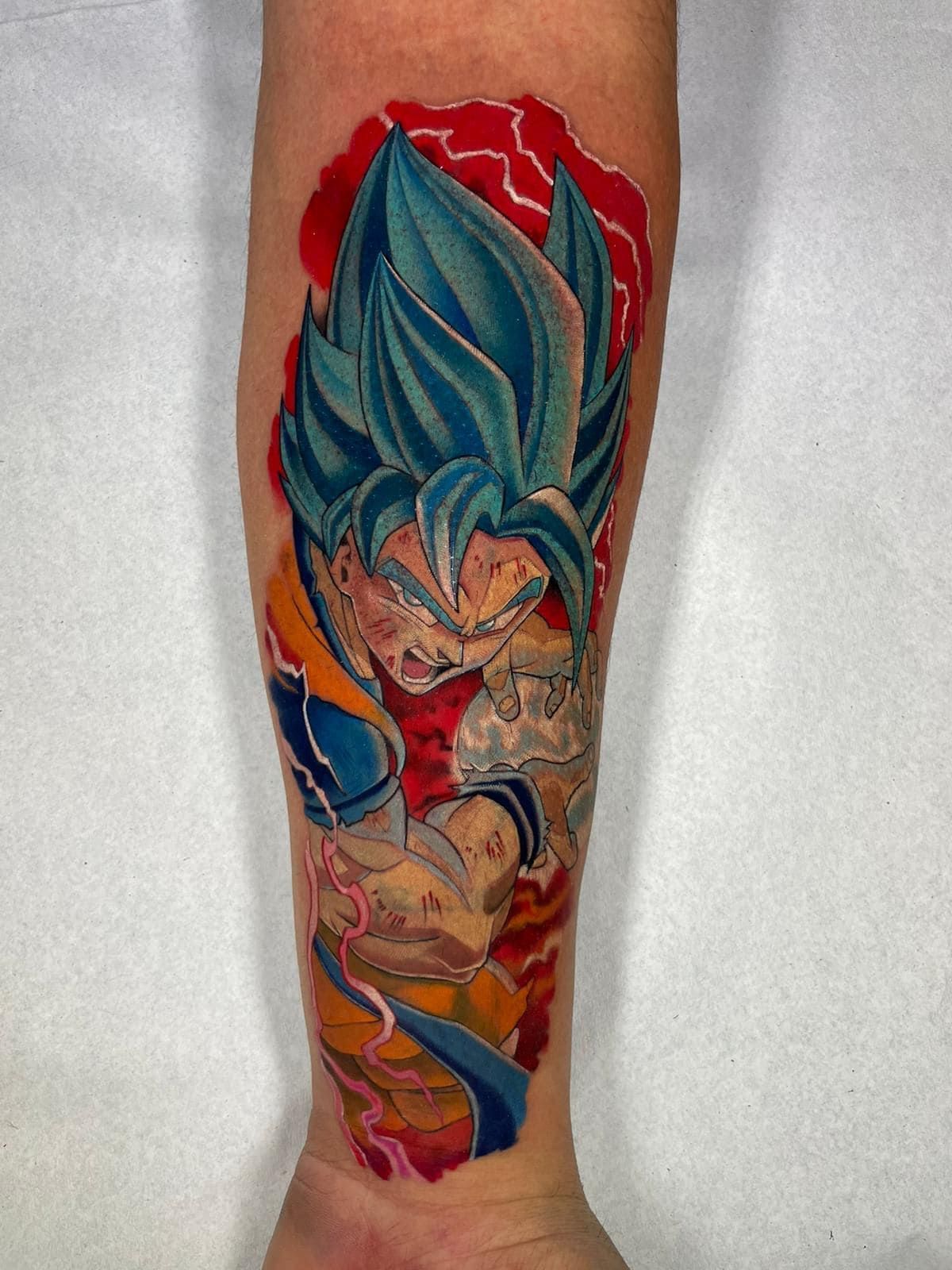 Tatuaje colorido estilo anime de un luchador de pelo azul en el antebrazo, con detalles en rojo y naranja.