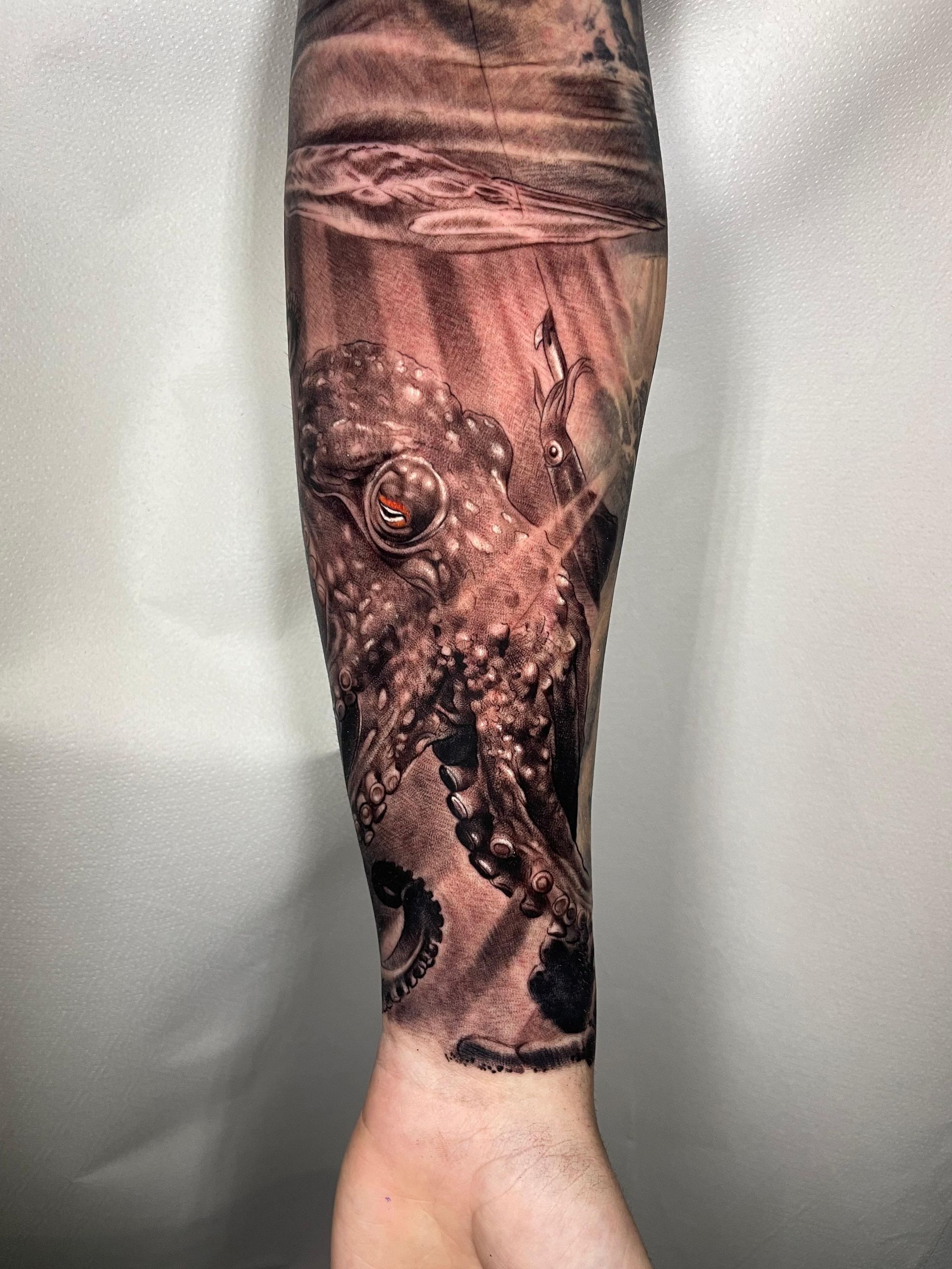 Pierna con un tatuaje en blanco y negro que representa un árbol y raíces sobre un fondo blanco.