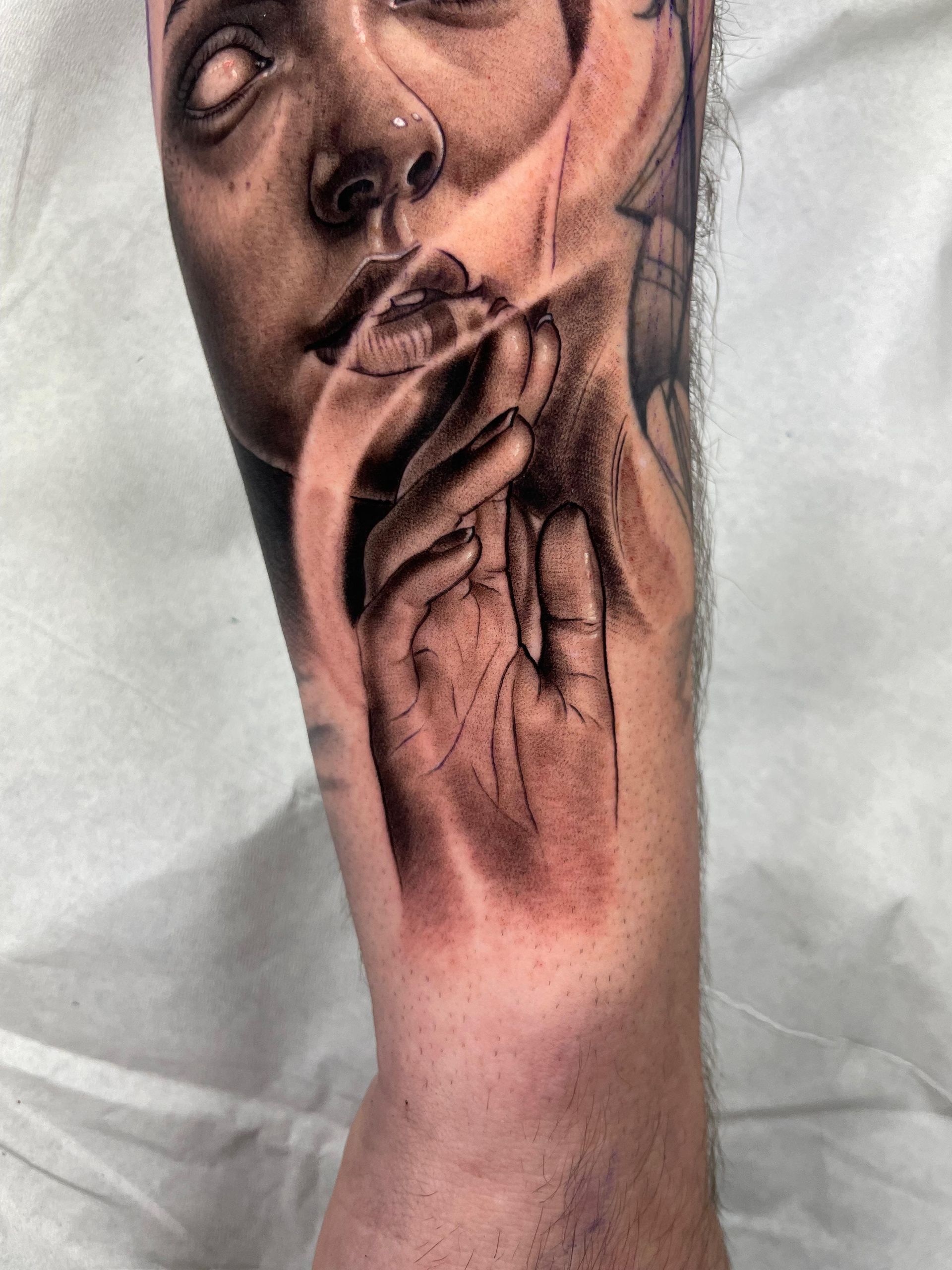 Primer plano de un tatuaje monocromático en la mano que muestra un rostro y manos rezando sobre la piel.