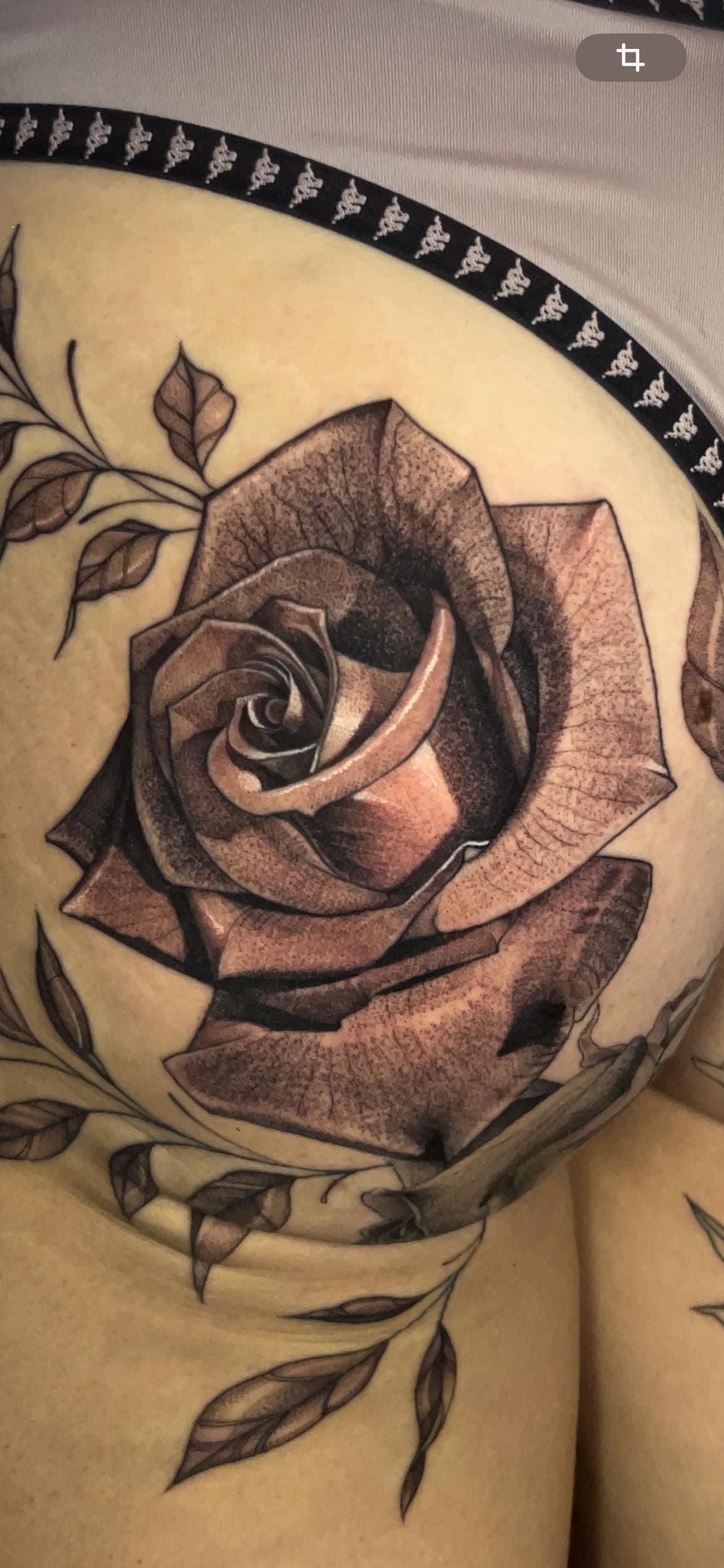 Primer plano de un tatuaje de rosa en blanco y negro con hojas en la piel.