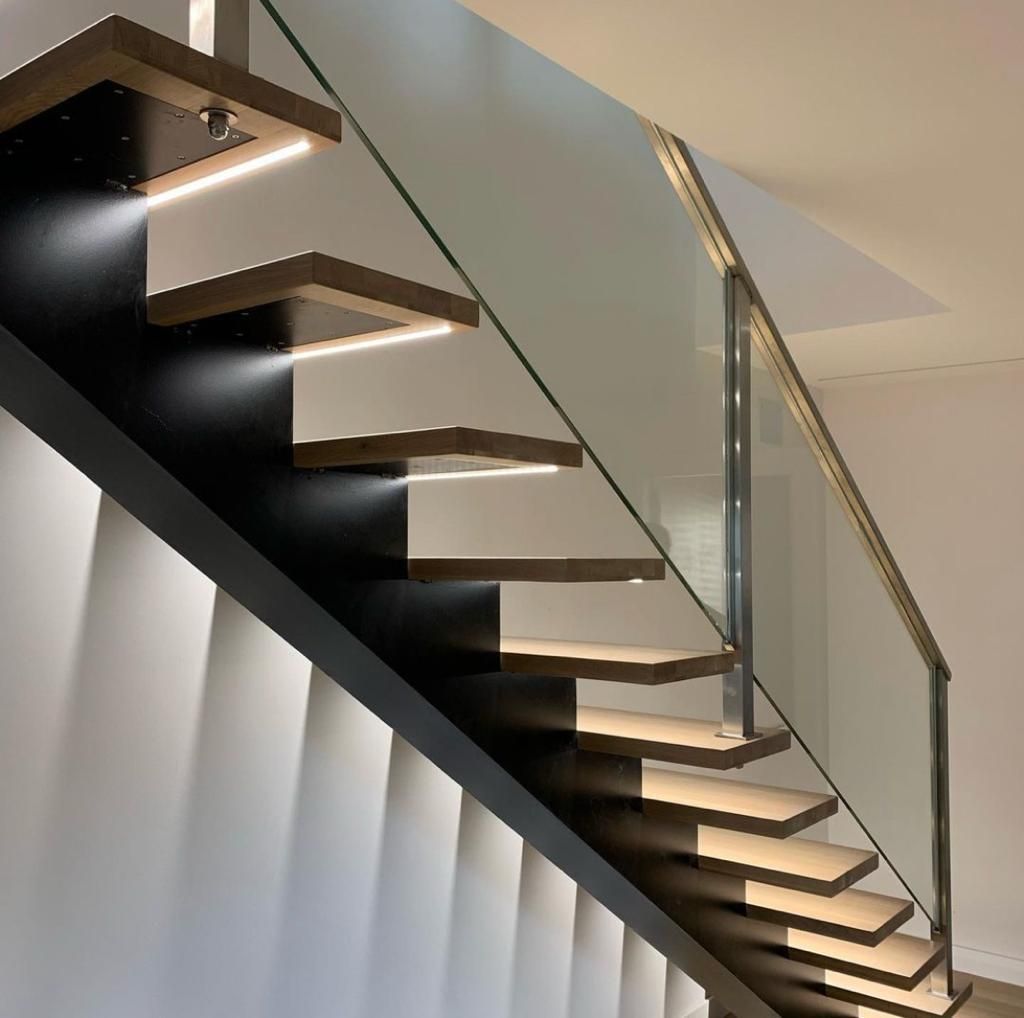 Escalera flotante de madera con iluminación debajo del escalón, barandilla de vidrio y viga de soporte negra