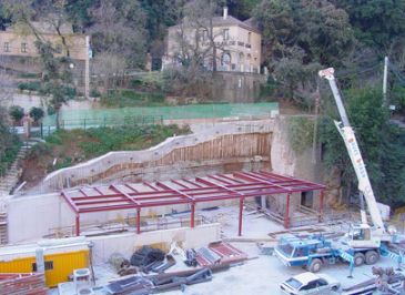 Sitio de construcción con una grúa, estructura de marco de metal y una ladera de fondo.