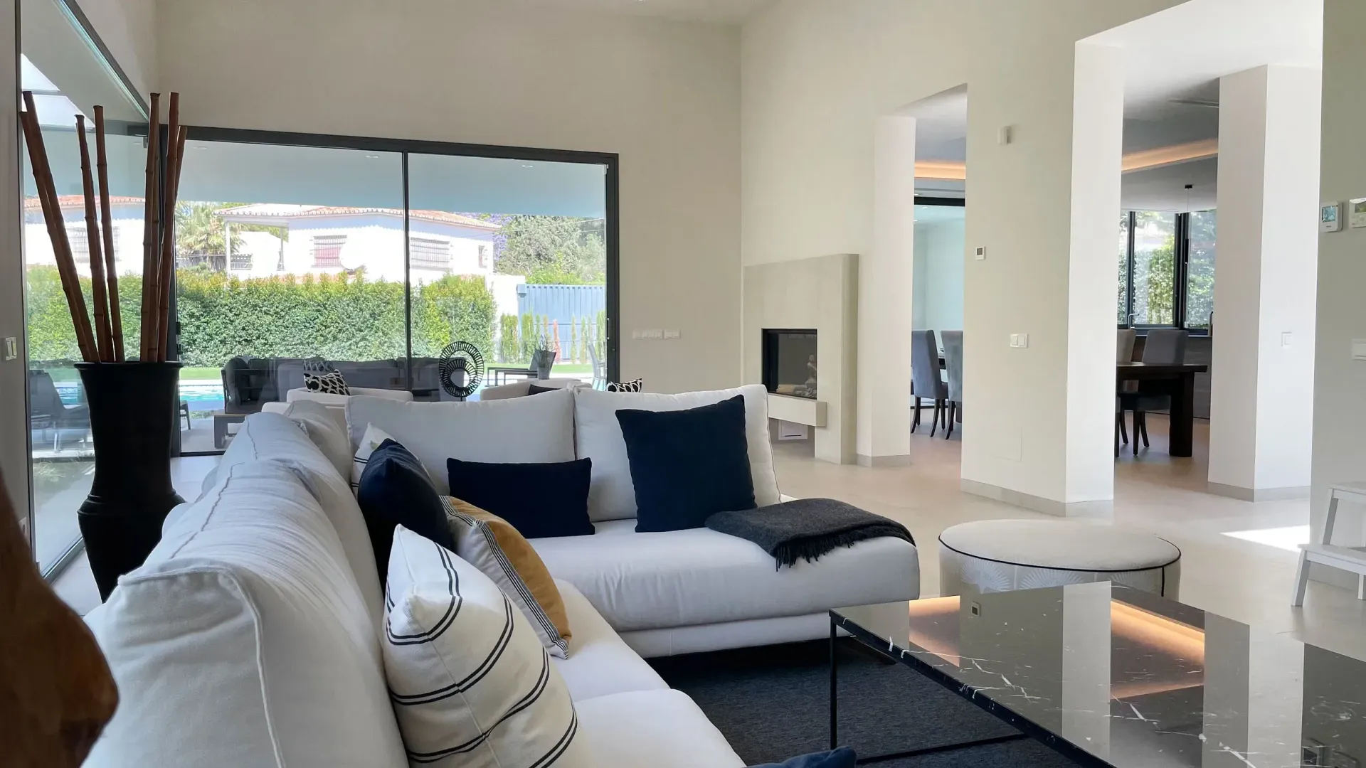 Moderna sala de estar con sofá blanco, grandes ventanales y chimenea.