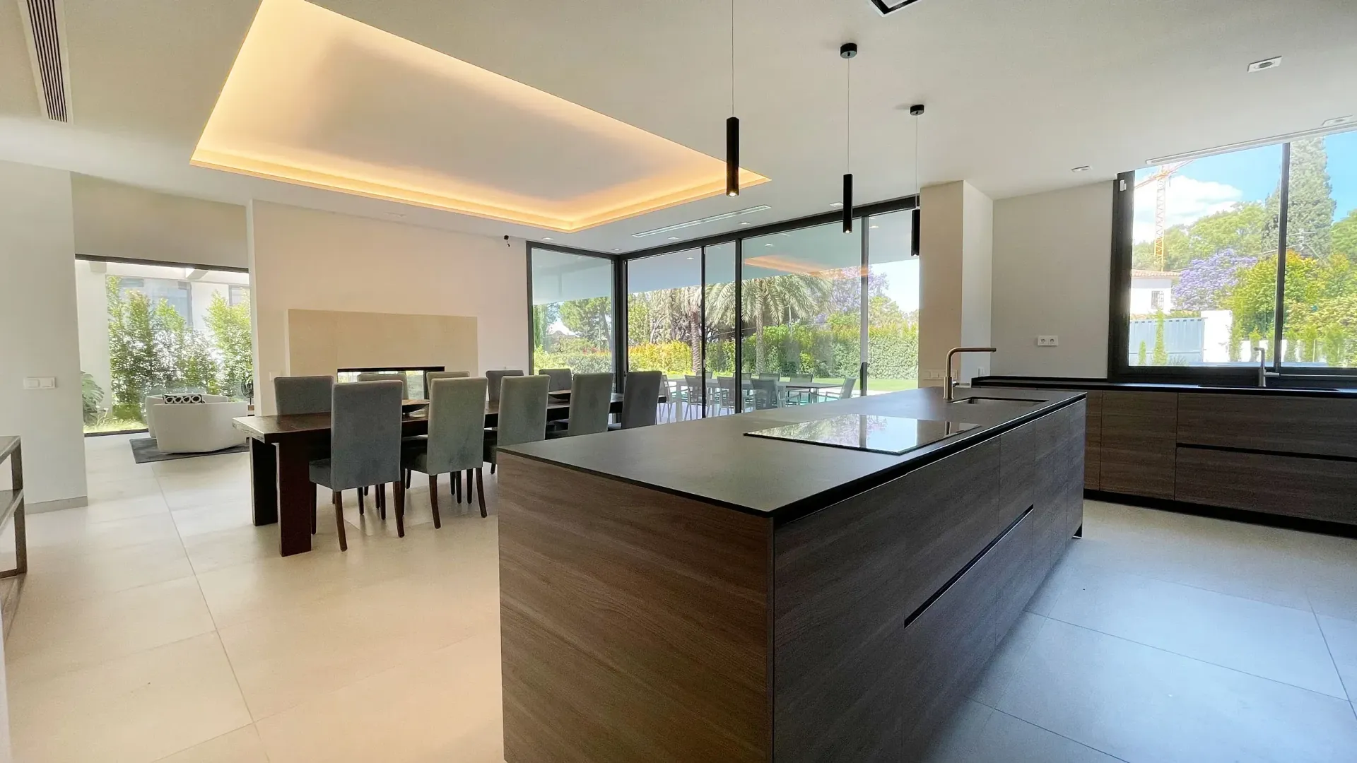 Cocina moderna con isla, comedor y grandes ventanales con vistas a los árboles.