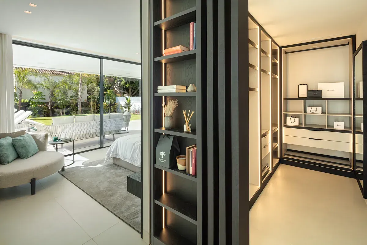 Dormitorio con armario abierto y estantería divisoria. Tonos neutros, vista al patio amueblado.