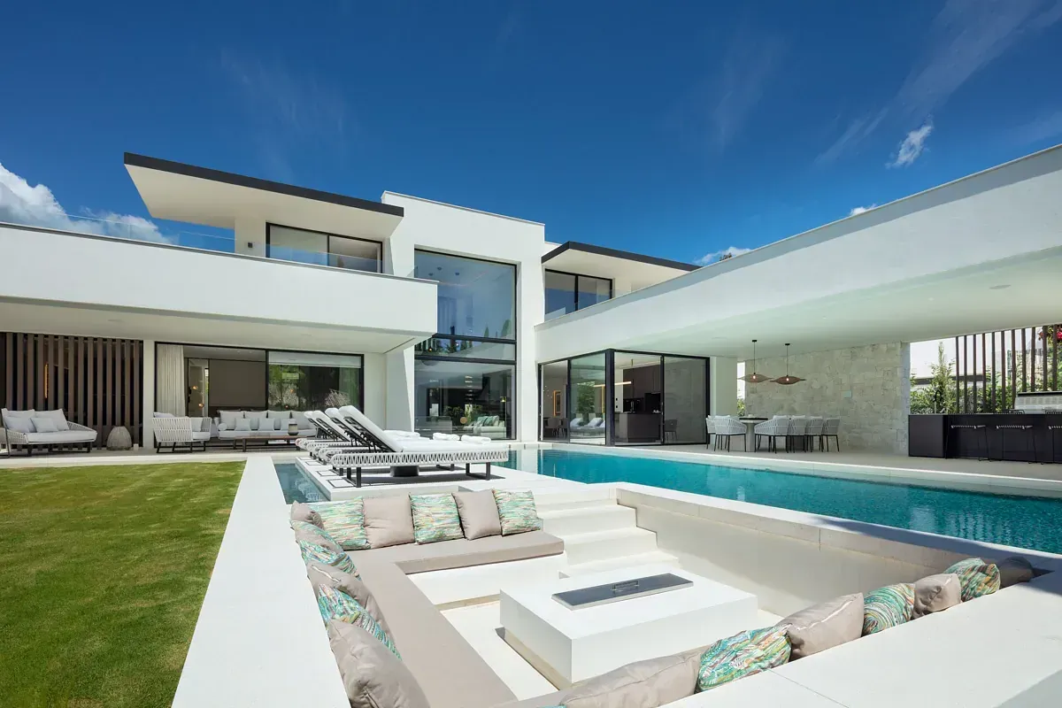 Moderna casa blanca con piscina, asientos al aire libre y exuberante césped verde.