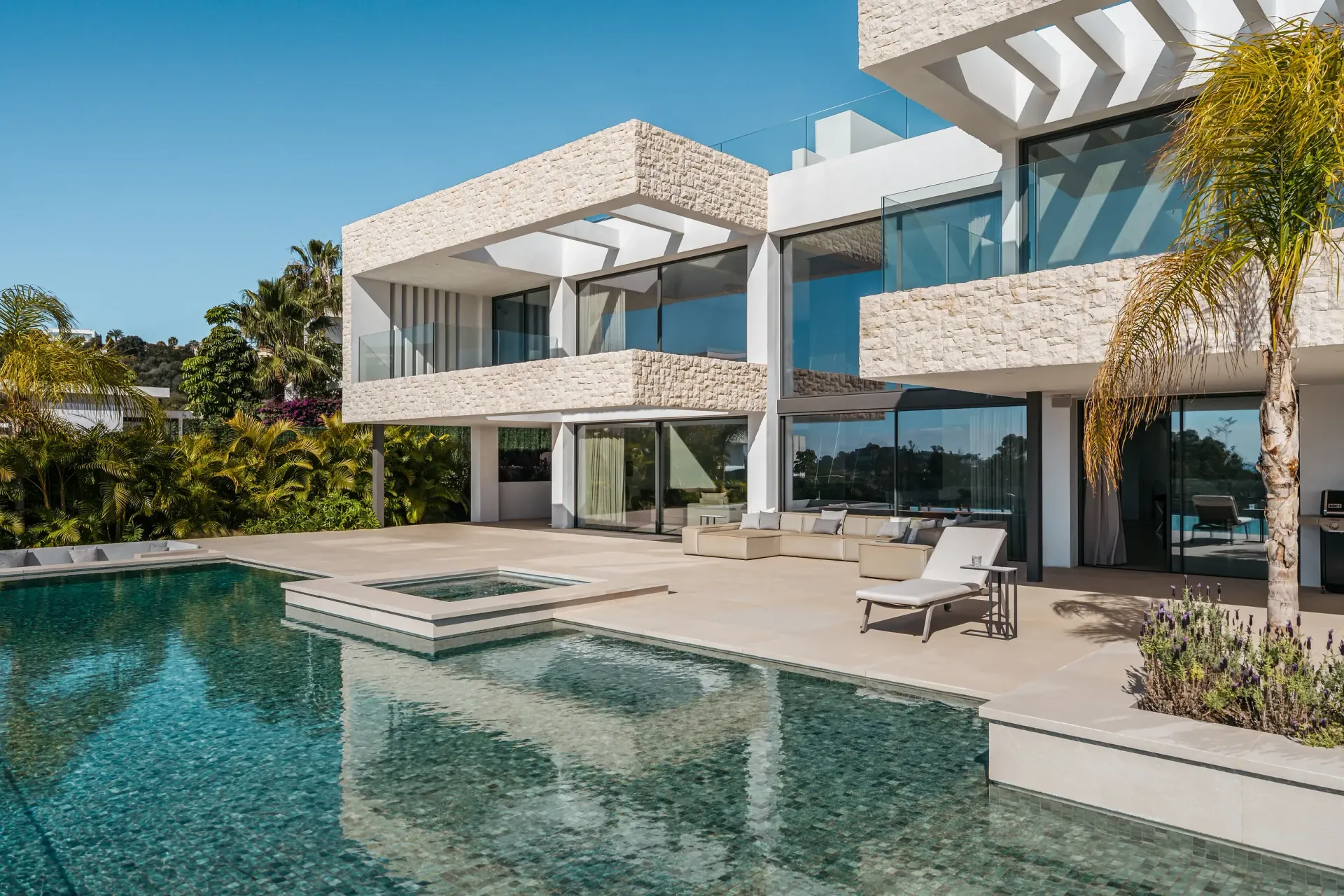 Moderna villa blanca con piscina, detalles en piedra y palmera bajo un cielo despejado.