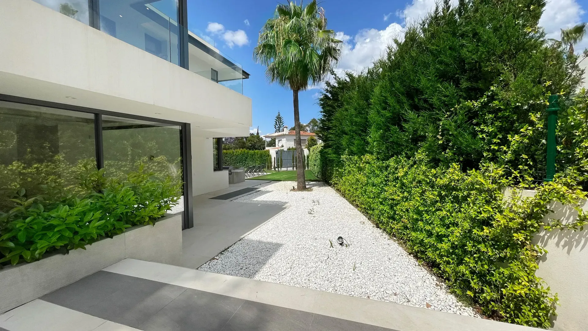 Exterior de casa moderna con grava blanca, setos verdes y un pequeño árbol.