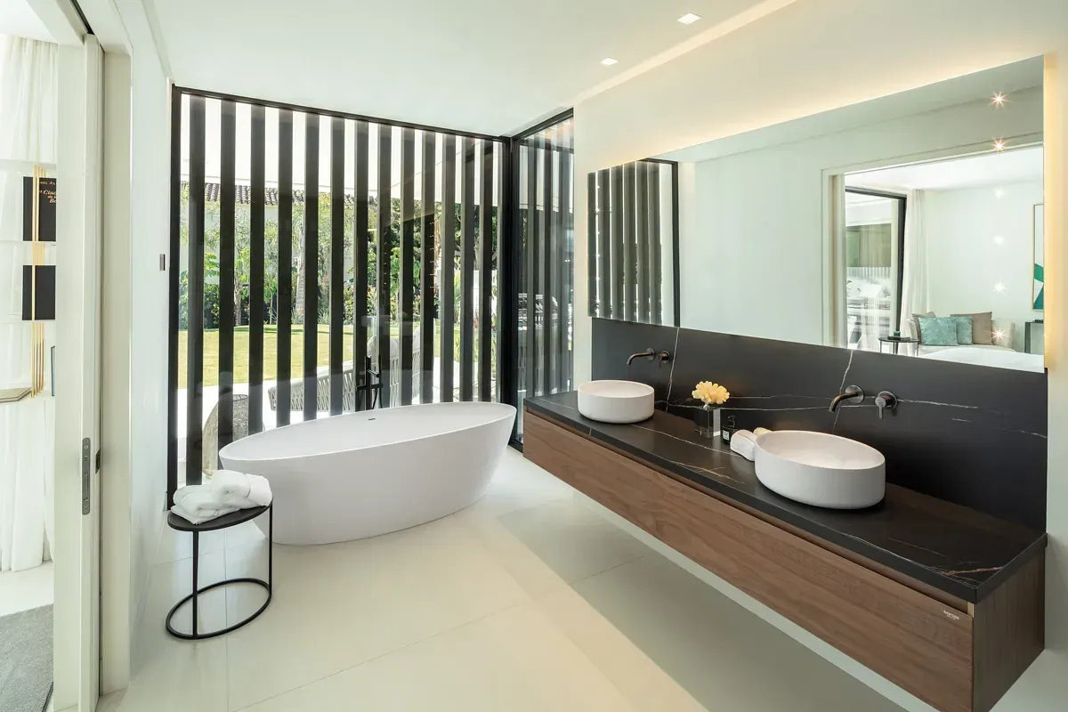 Baño moderno con bañera independiente, tocador flotante y gran ventanal con persianas verticales.