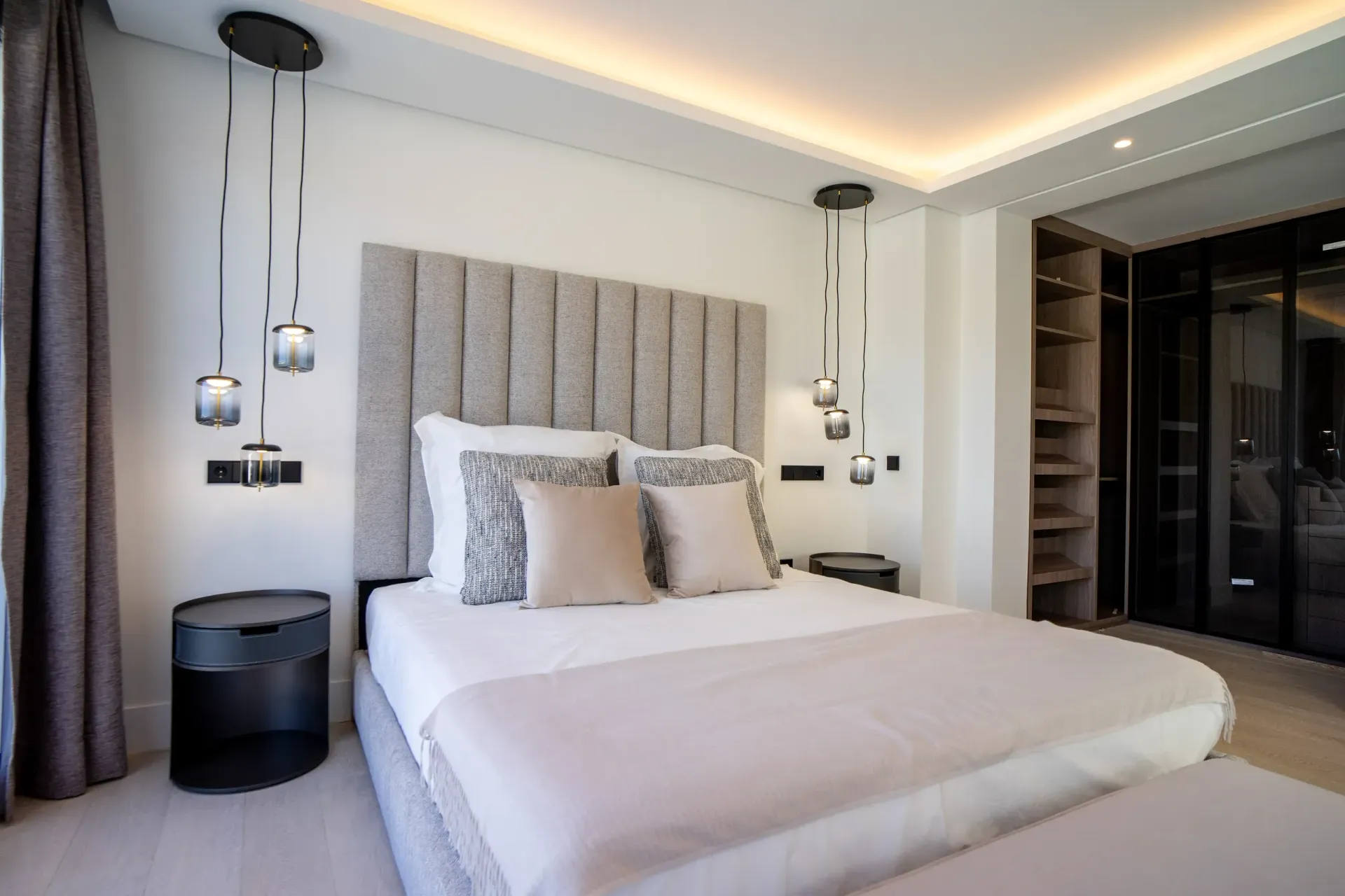 Dormitorio con cama, mesitas de noche, lámparas colgantes, cabecero y vestidor.