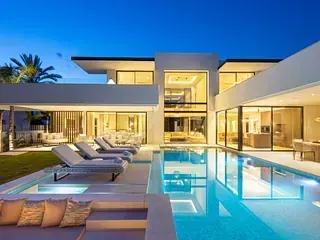 Moderna casa de lujo con piscina, tumbonas y paredes de cristal al anochecer.