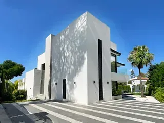 Moderna villa blanca con detalles negros y palmeras, contra un cielo azul brillante.