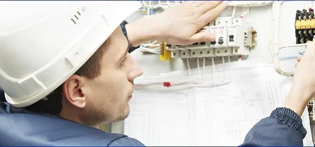 Un hombre que lleva un casco está trabajando en una caja eléctrica.