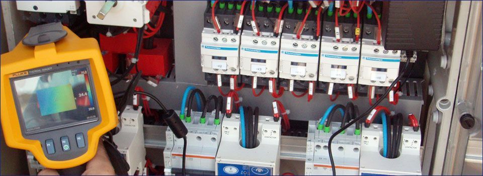 Una persona sostiene un termómetro Fluke frente a un panel eléctrico.